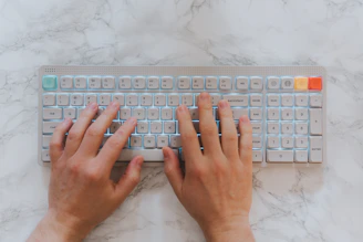 Hands typing on a backlit keyboard on a marble surface