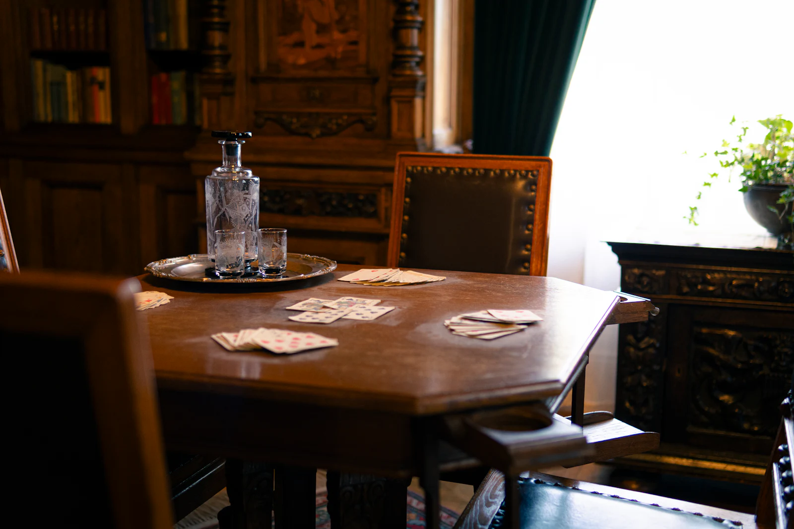 Playing cards and a cut glass decanter on a dark wood table.