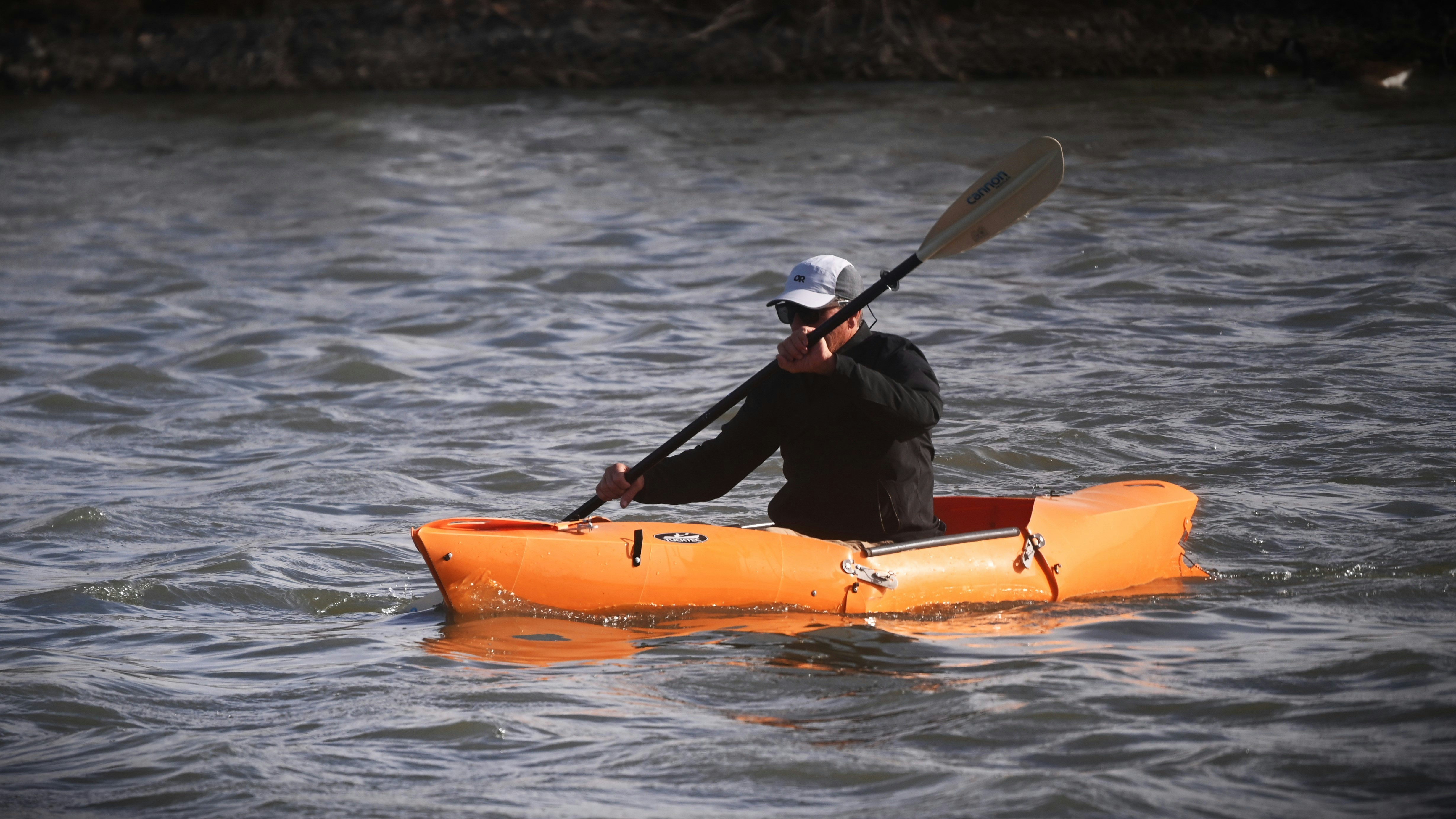Man paddling an orange kayak on wavy water
