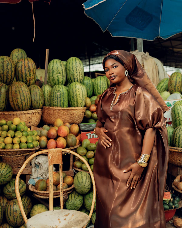 West African woman in traditional dress at a vibrant fruit market