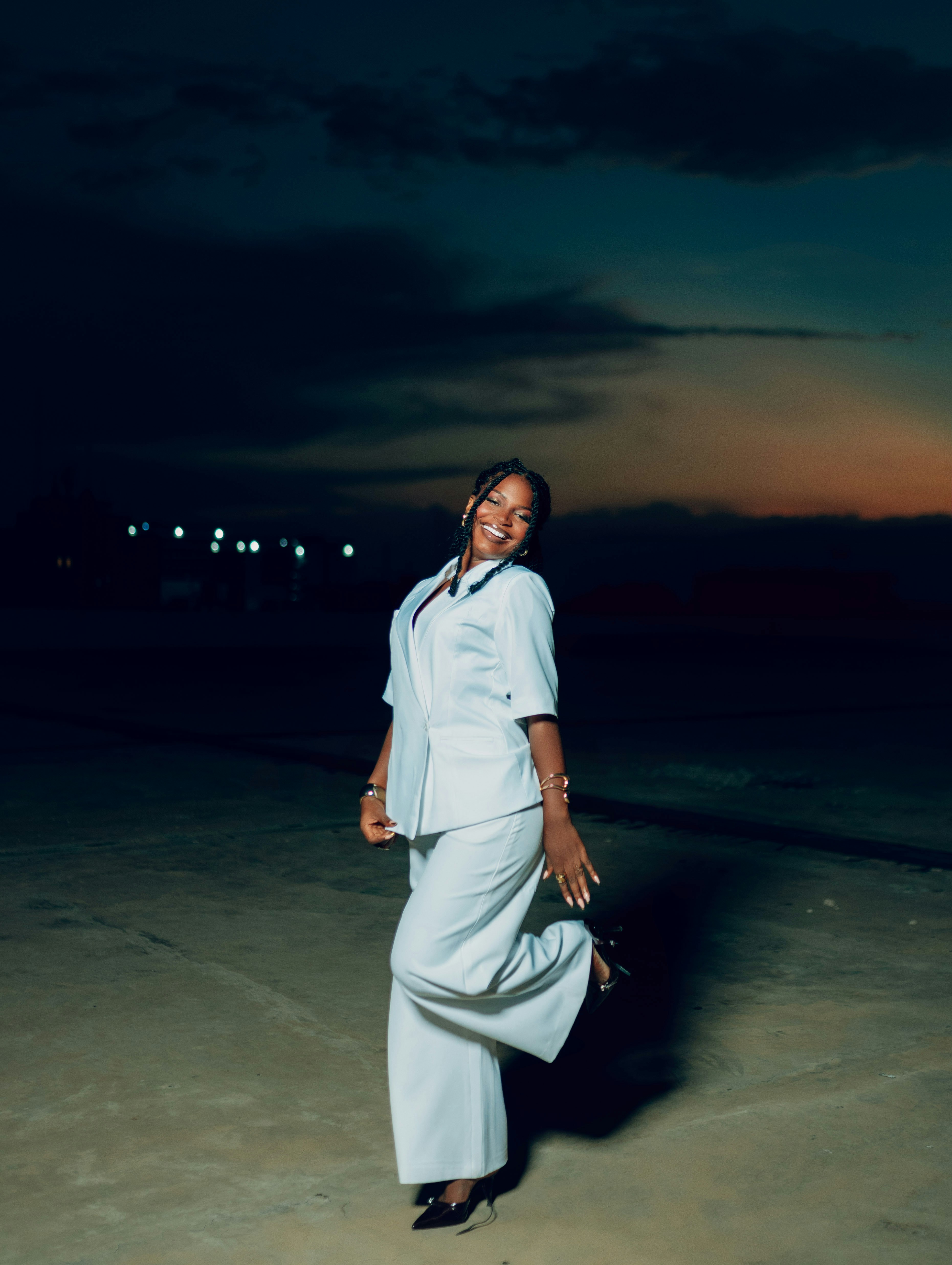 A woman in a white suit poses at dusk