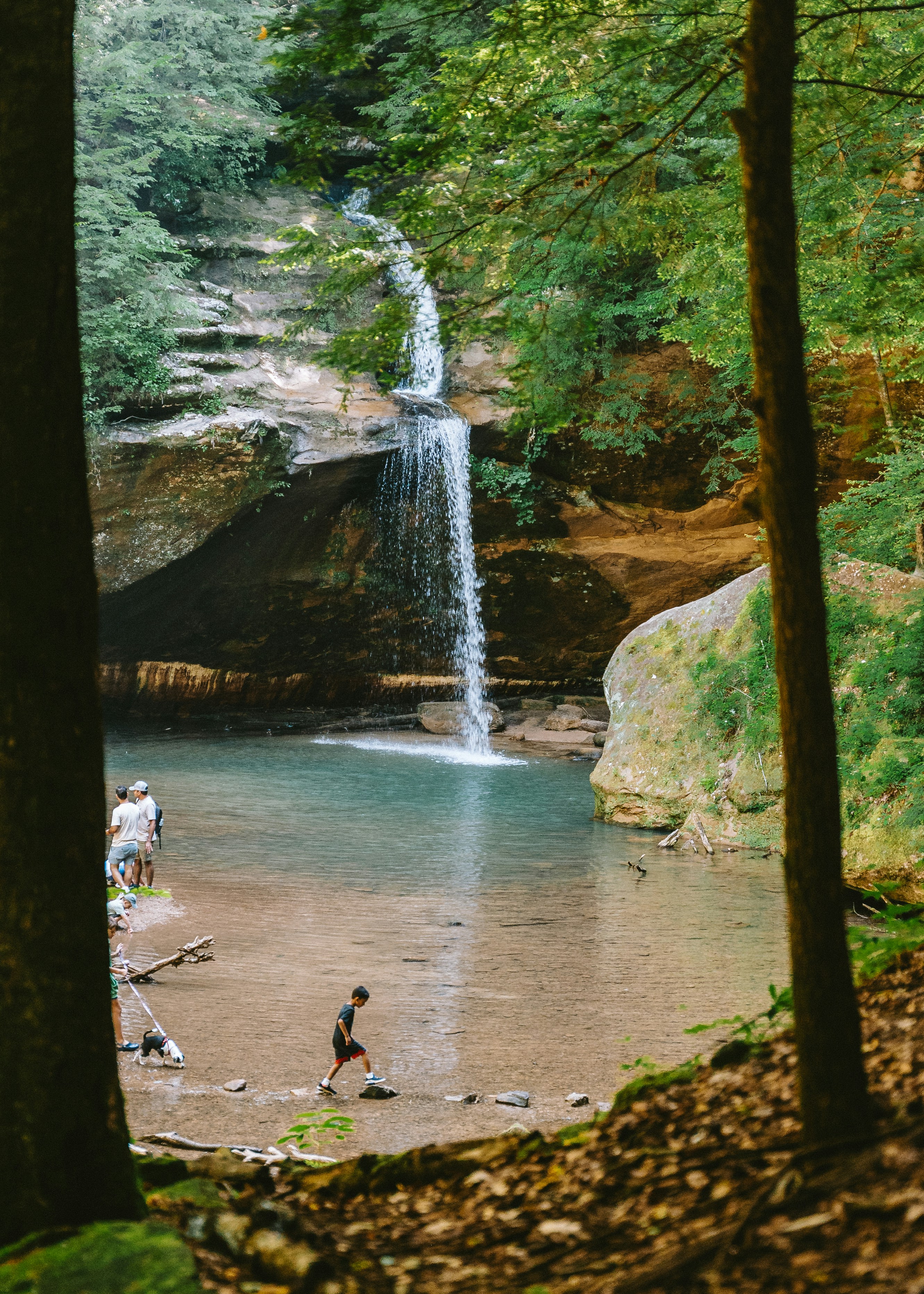 Uma pessoa atravessa um riacho perto de uma cachoeira.