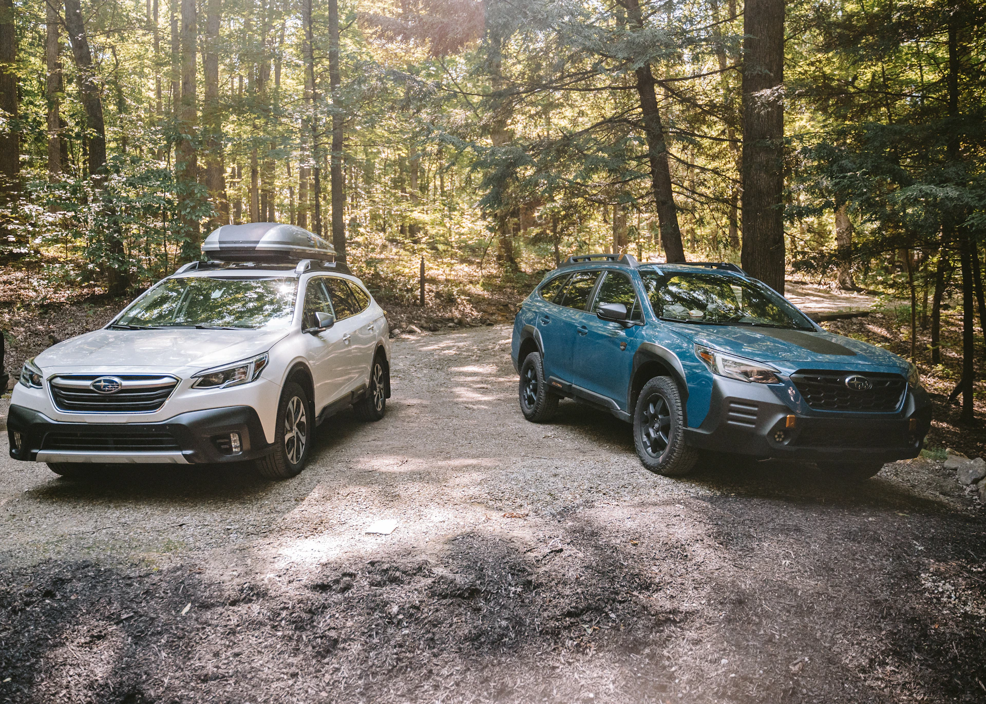 Two subaru outbacks parked on a dirt road.