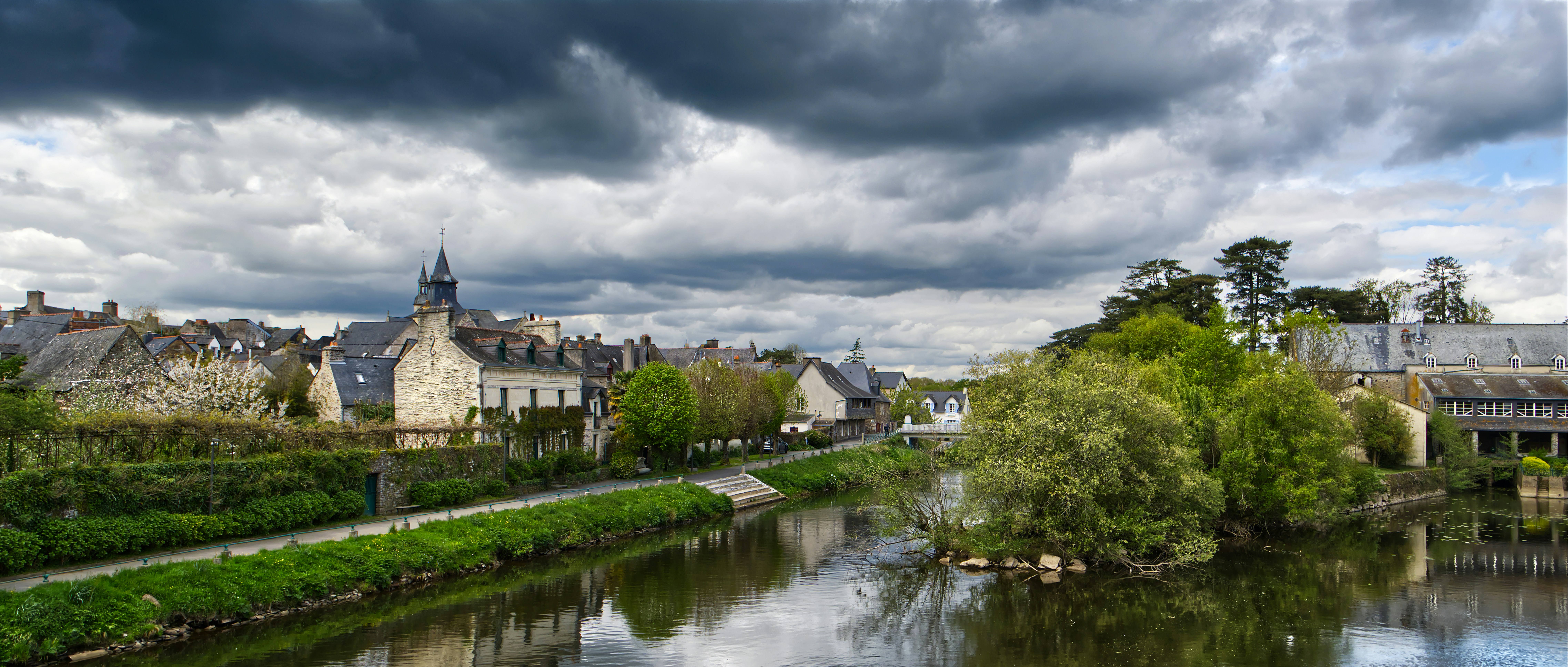 River flows past a european town under dramatic clouds