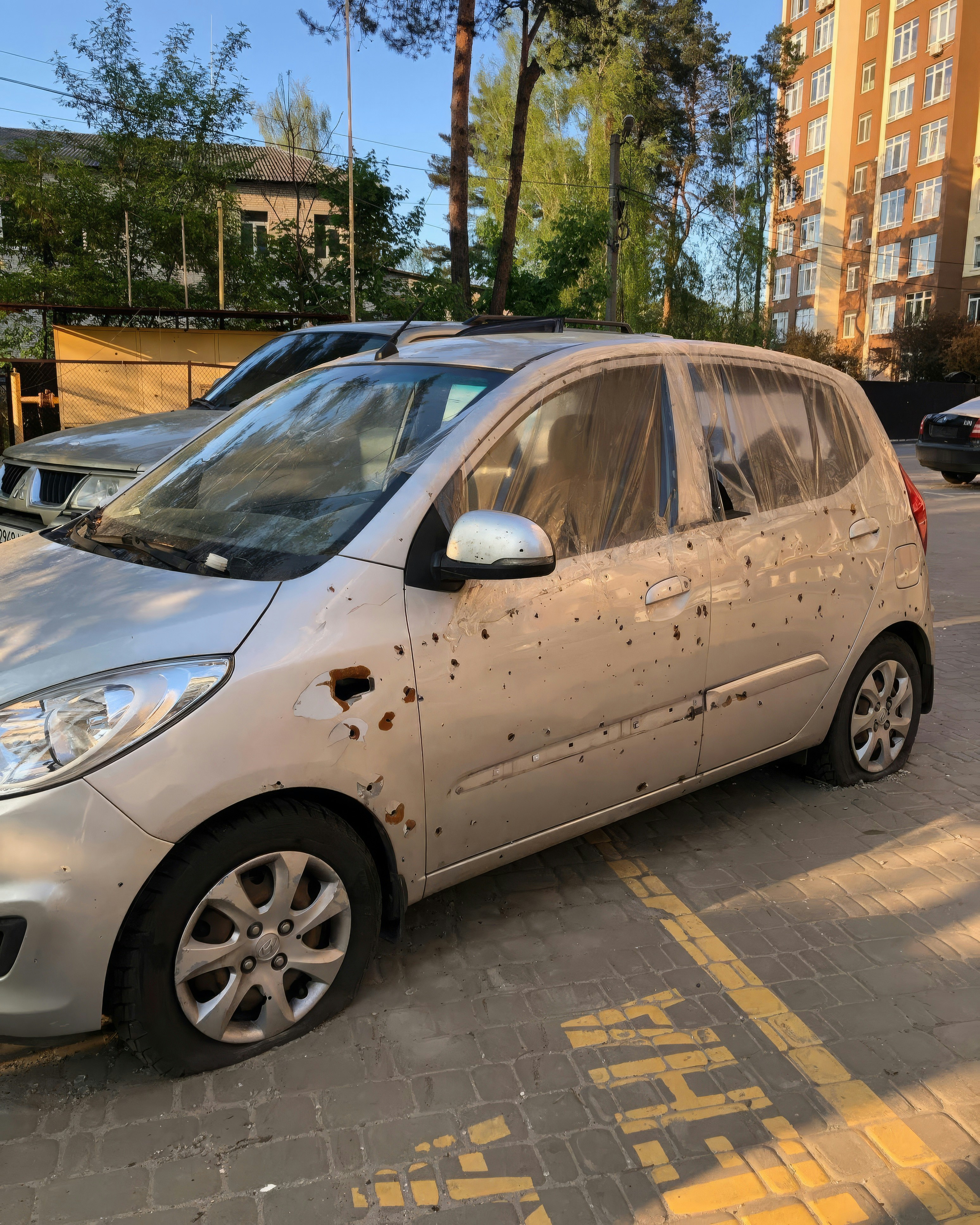 Silbernes Auto mit platten Reifen und Einschusslöchern.