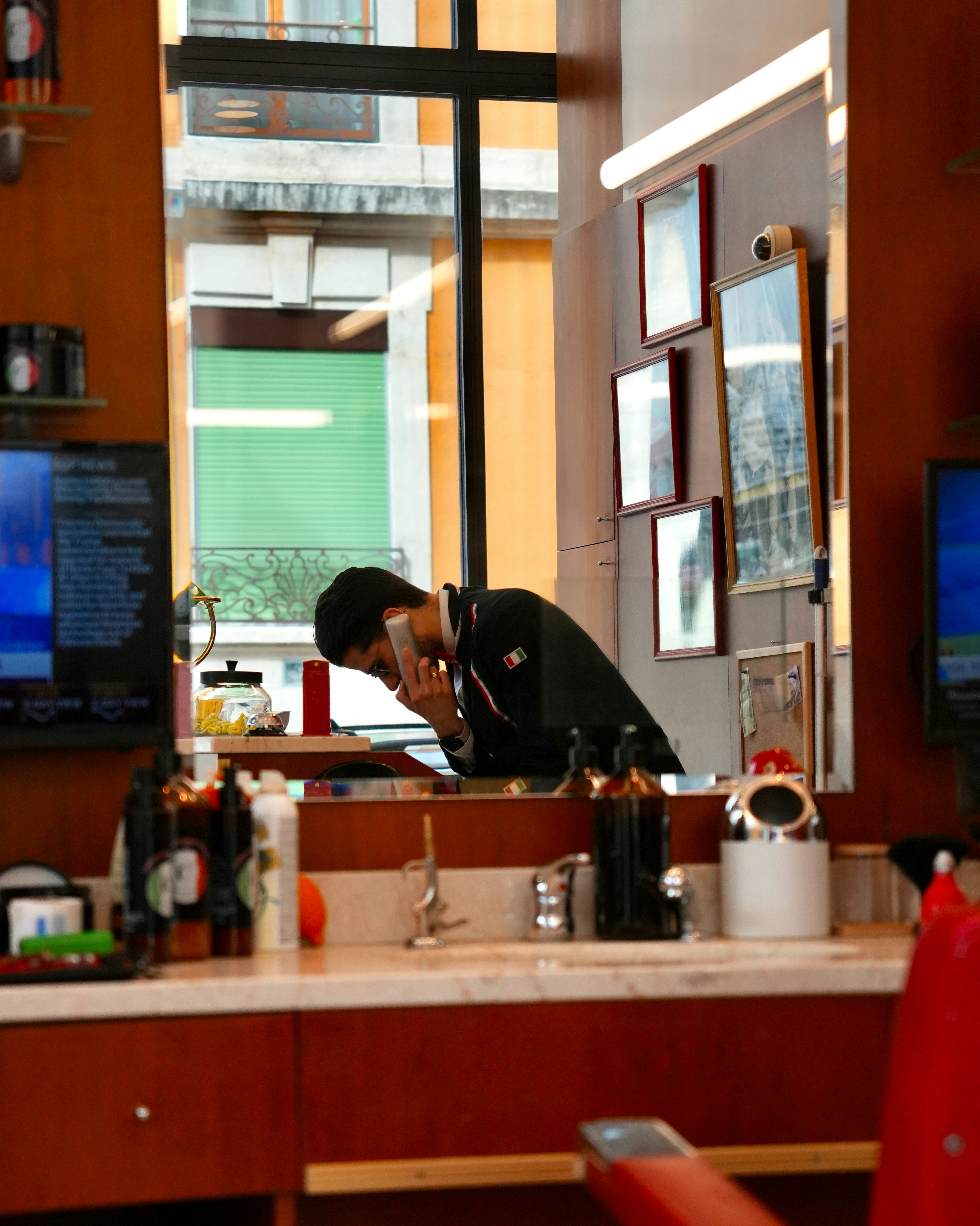 Barber shaving a client in a mirror reflection.