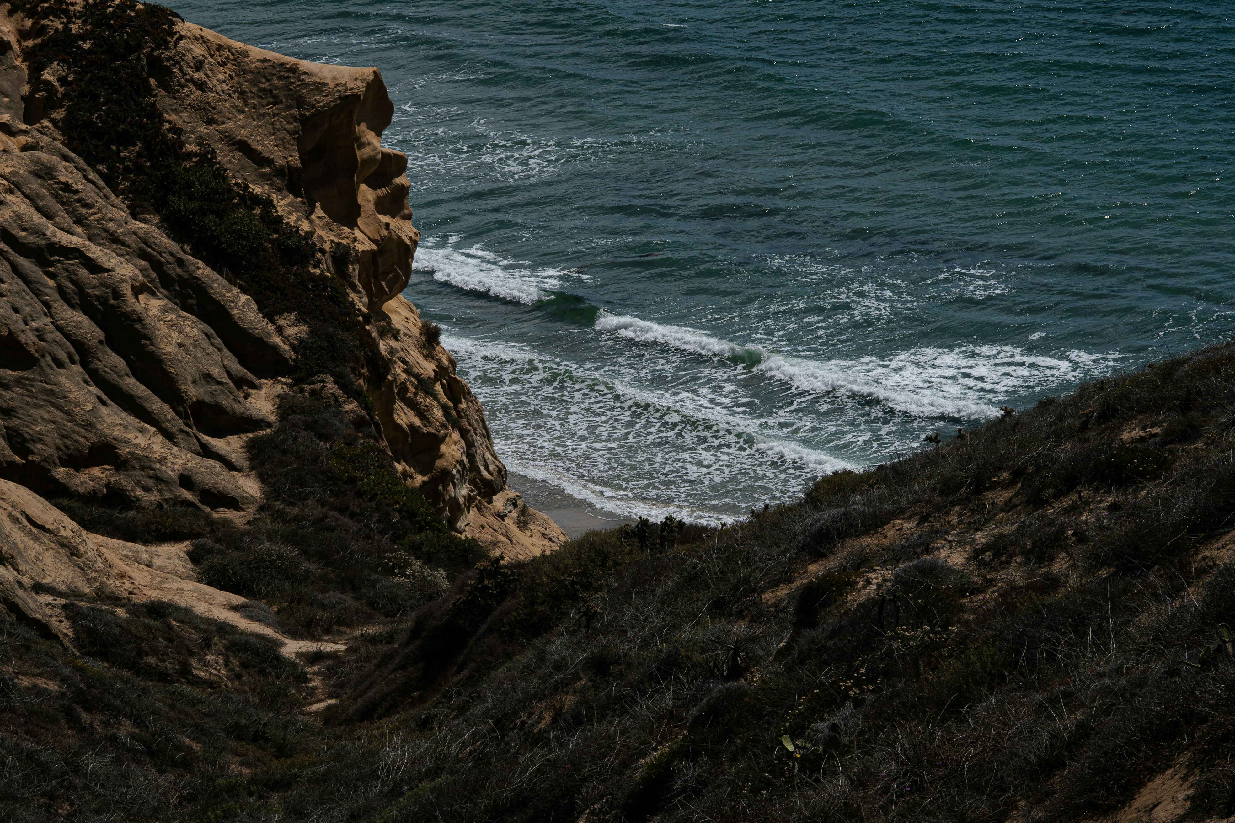 Las olas rompen en una playa de arena bajo un acantilado rocoso.