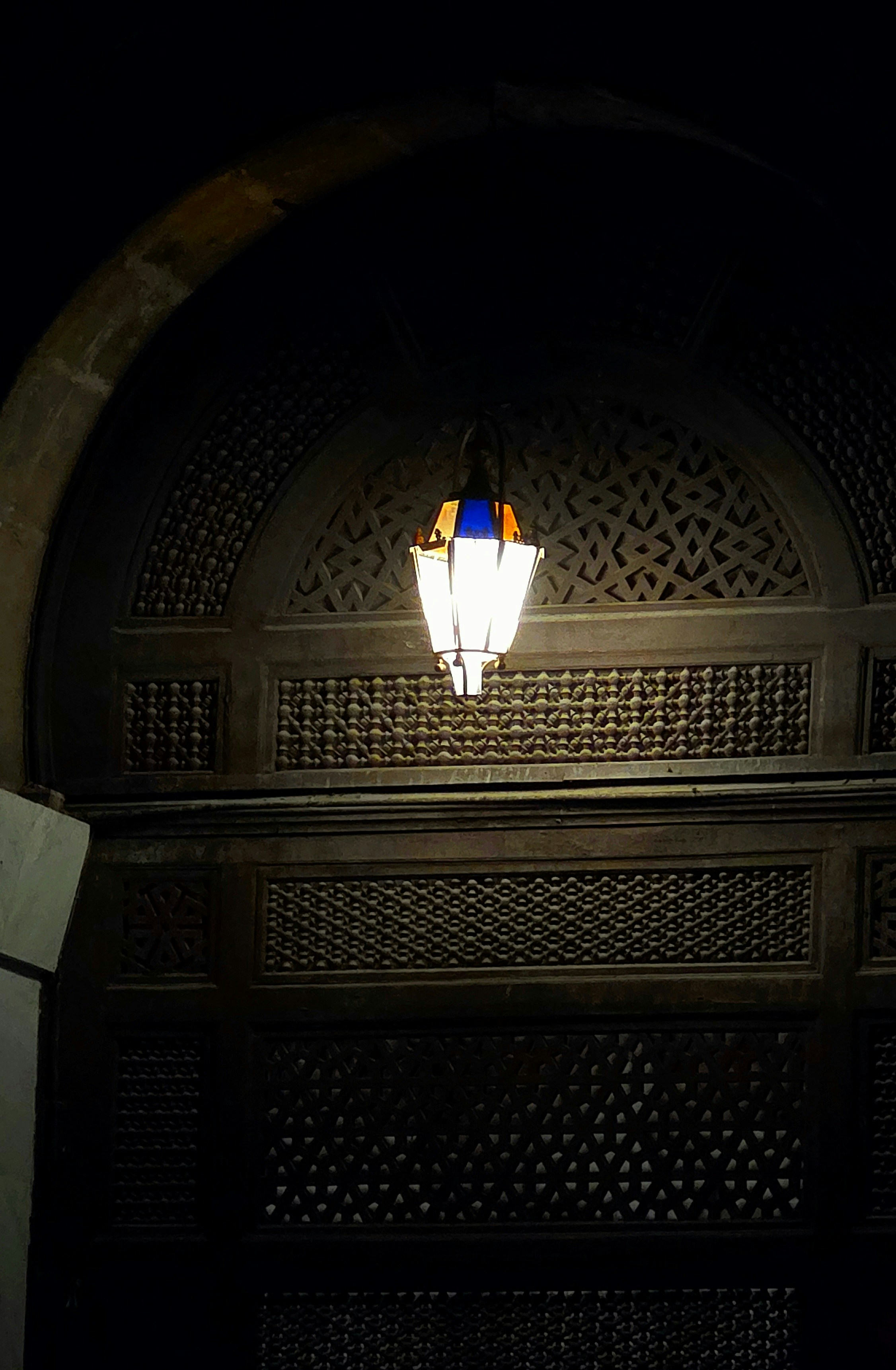 Uma lanterna decorativa está pendurada em um cômodo escuro e ornamentado.