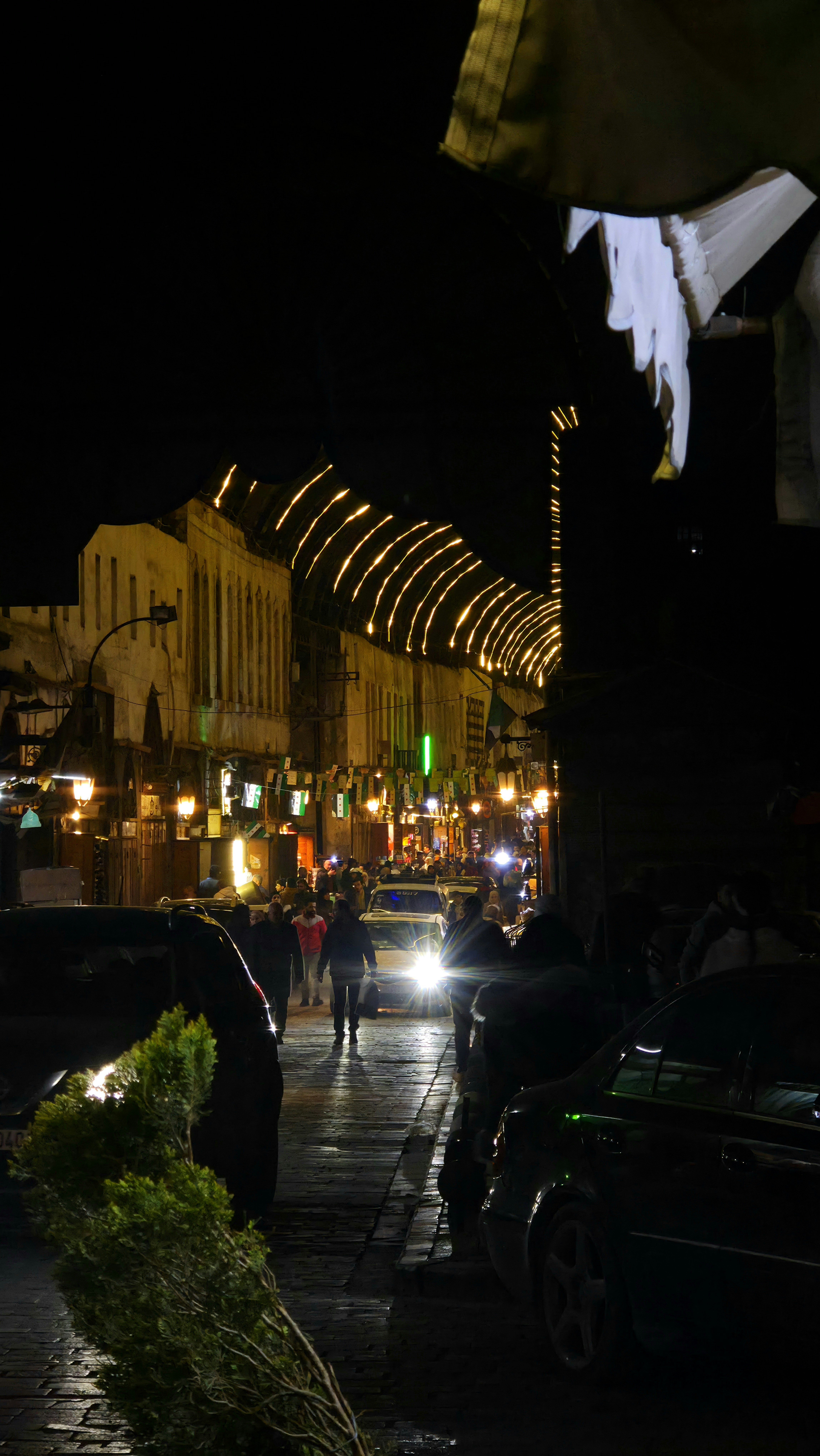 Pessoas caminhando na rua à noite com luzes.