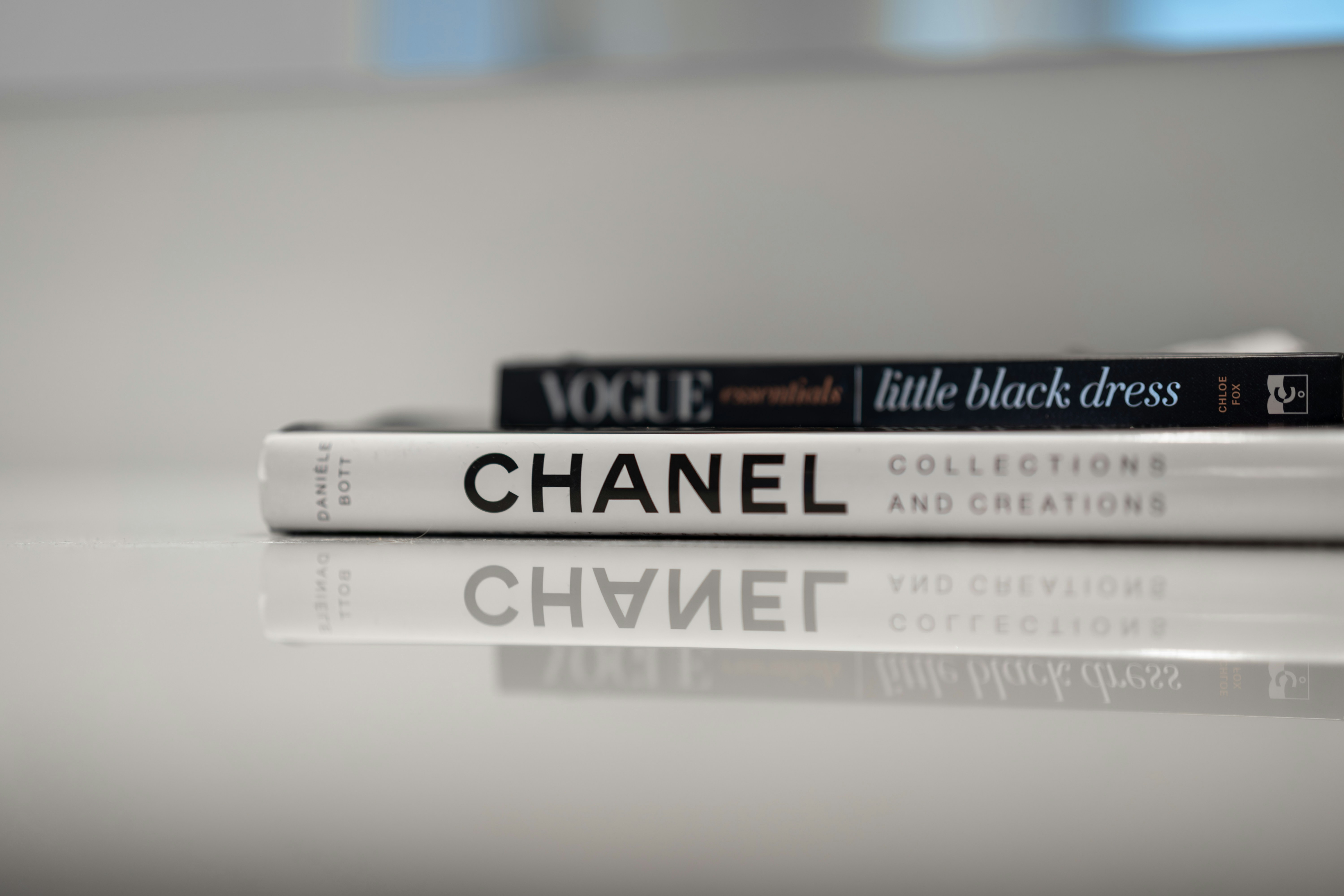 Chanel and vogue books stacked on a reflective surface.