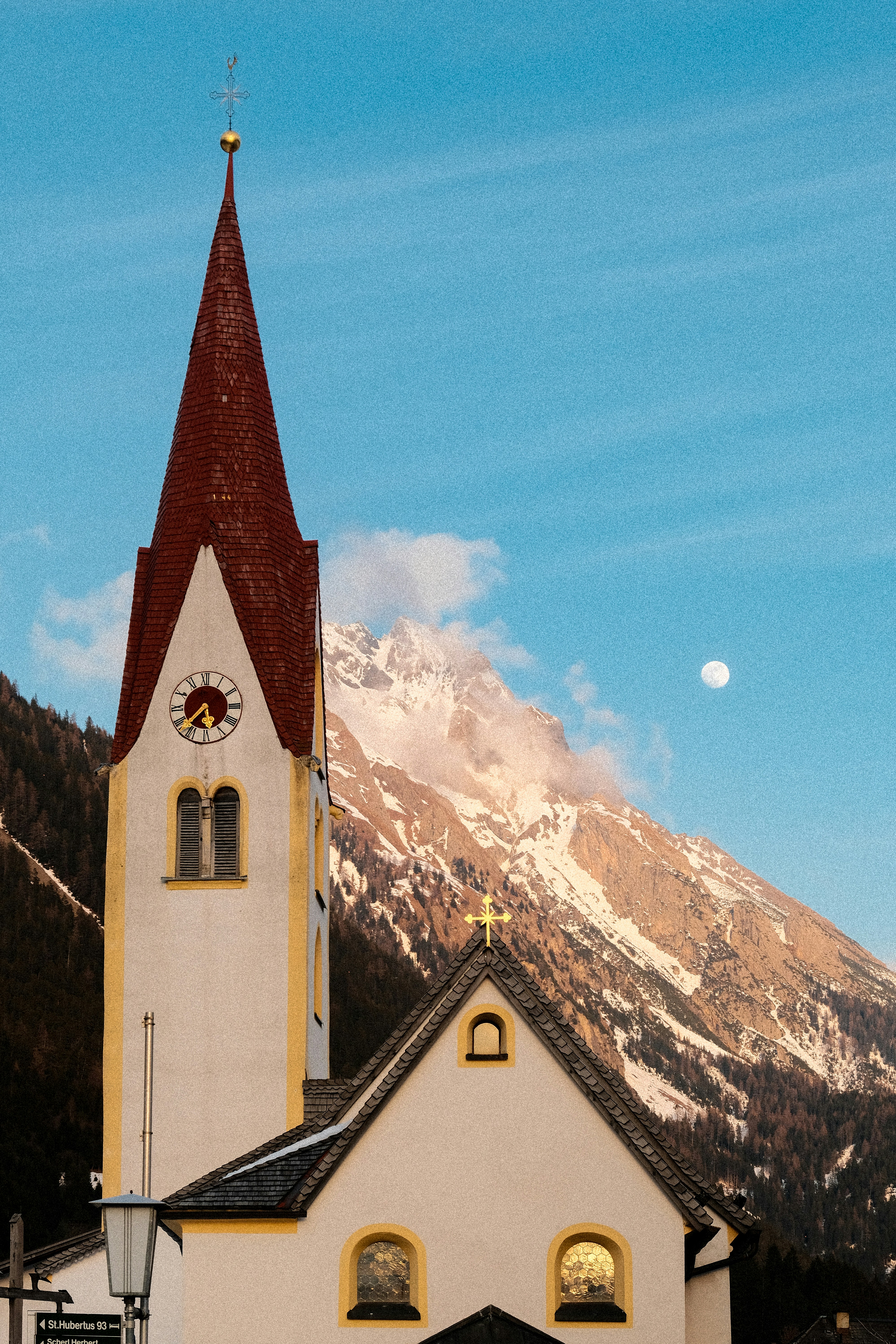 Kirchturm vor schneebedeckten Bergen und Mond.
