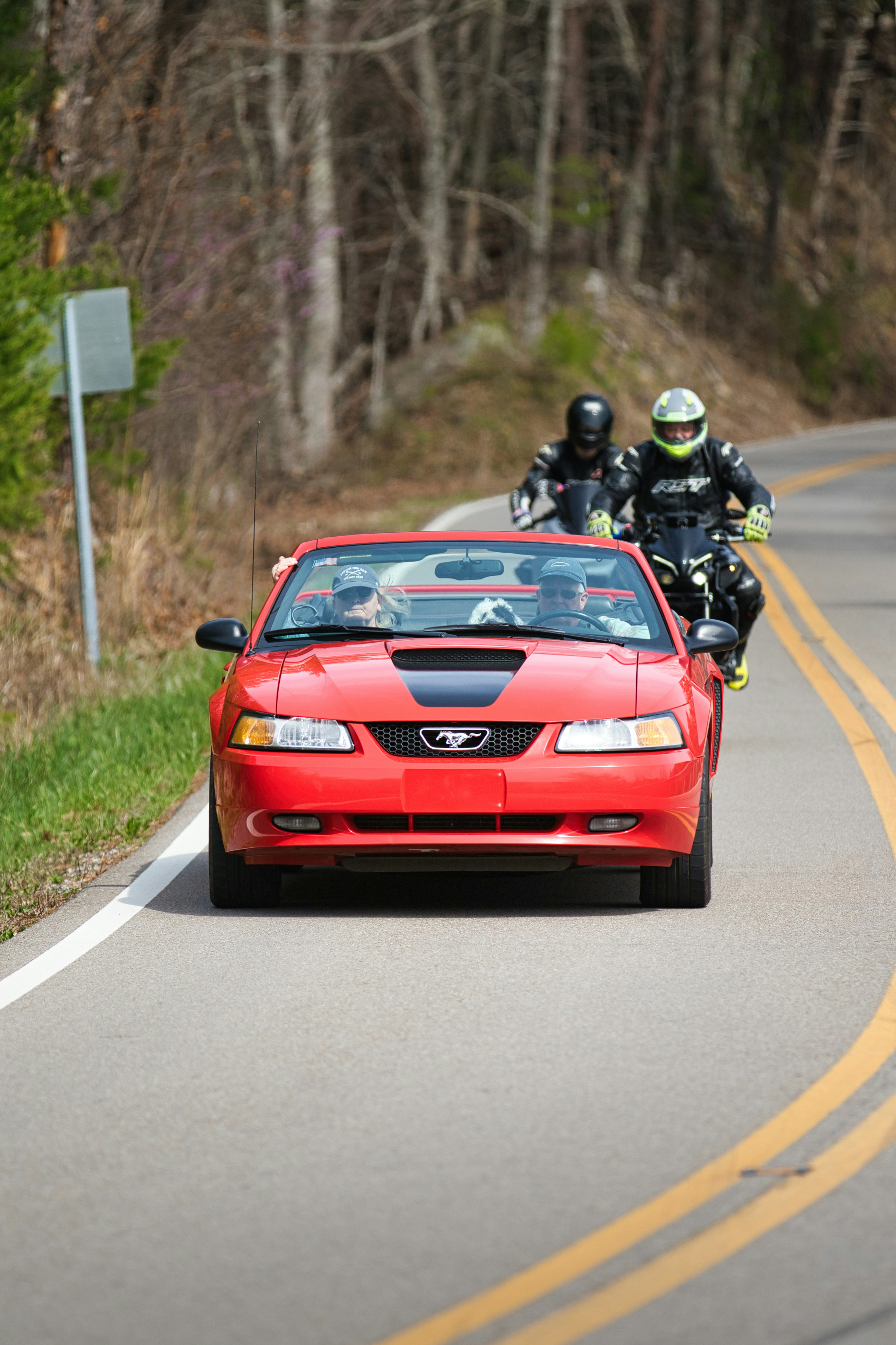 Red convertible mustang driving on a road