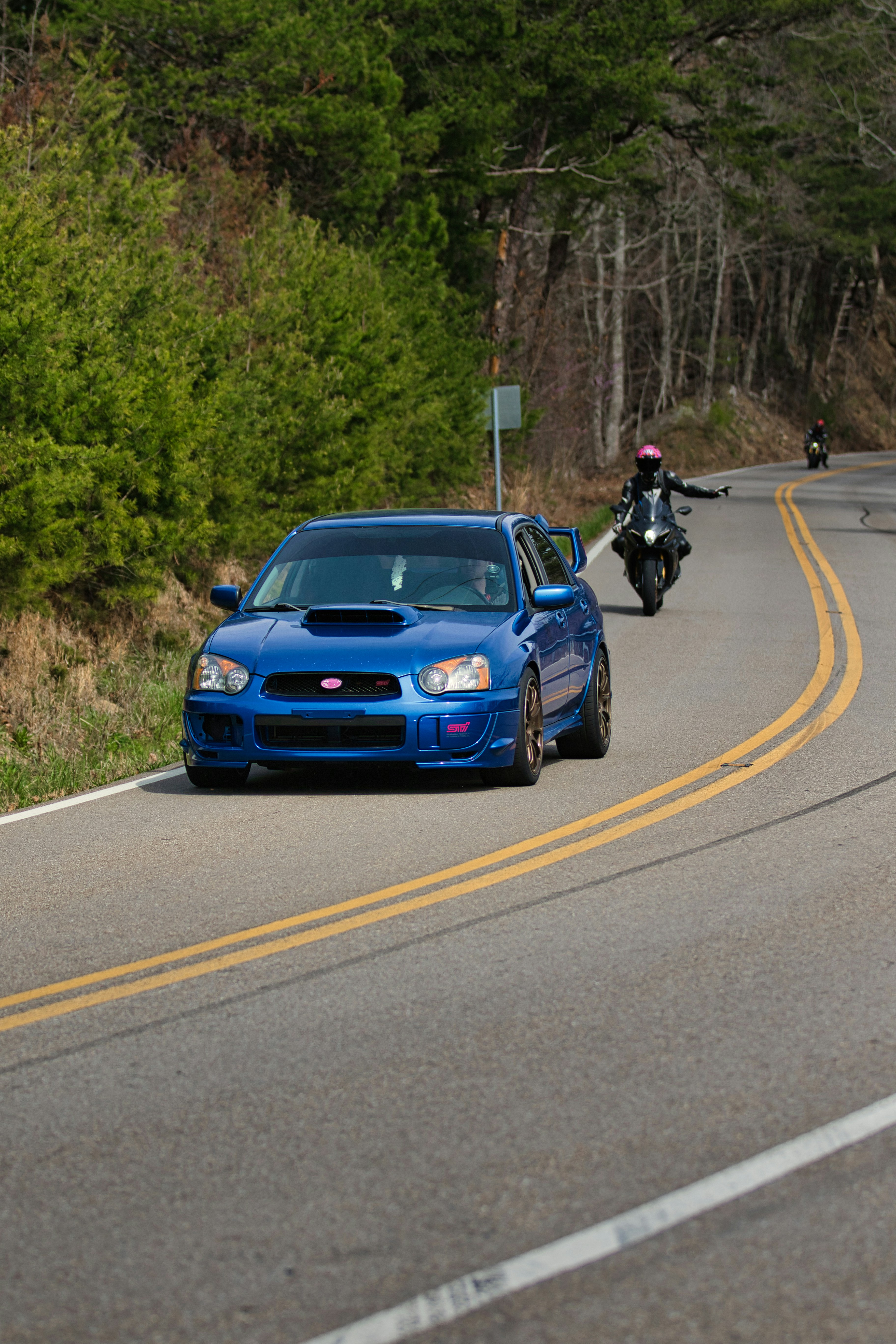 Blauer Subaru WRX fährt auf einer kurvigen Straße mit Motorrad
