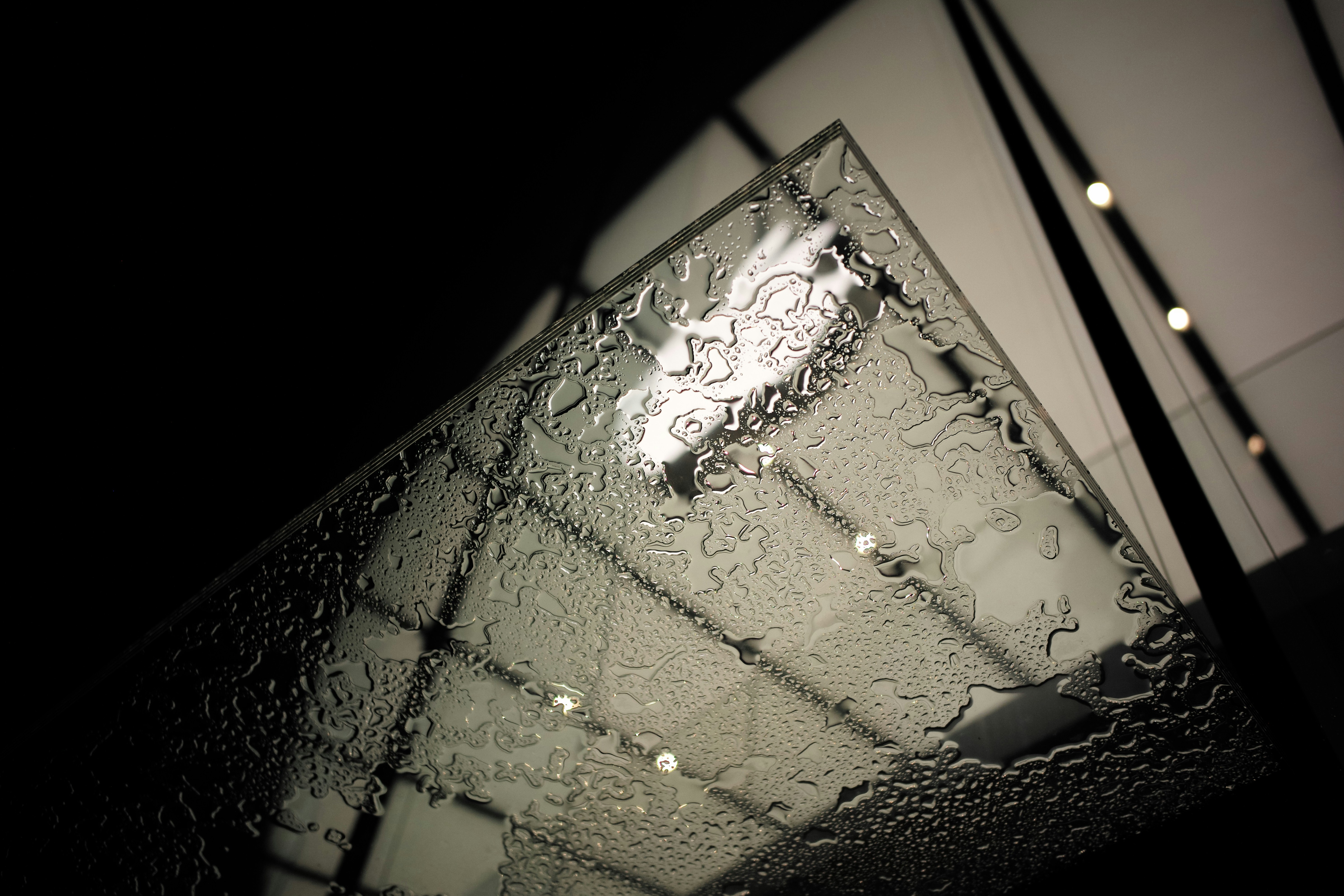 Water droplets on a glass surface with ceiling lights.
