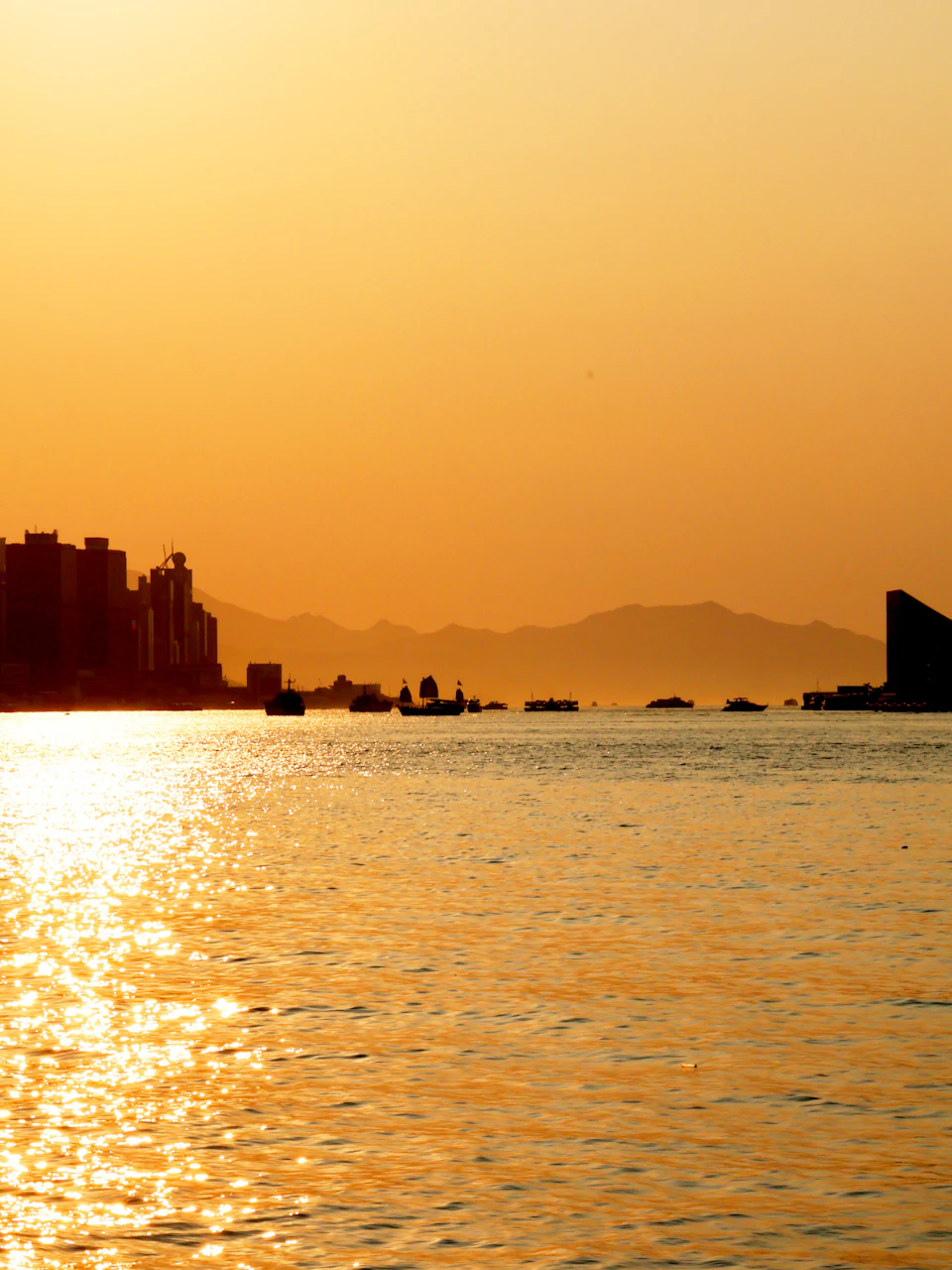 Serene sunset over calm waters with boats and distant mountains in warm orange hues