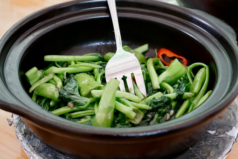 A fork stirring a pot of dark cooked greens
