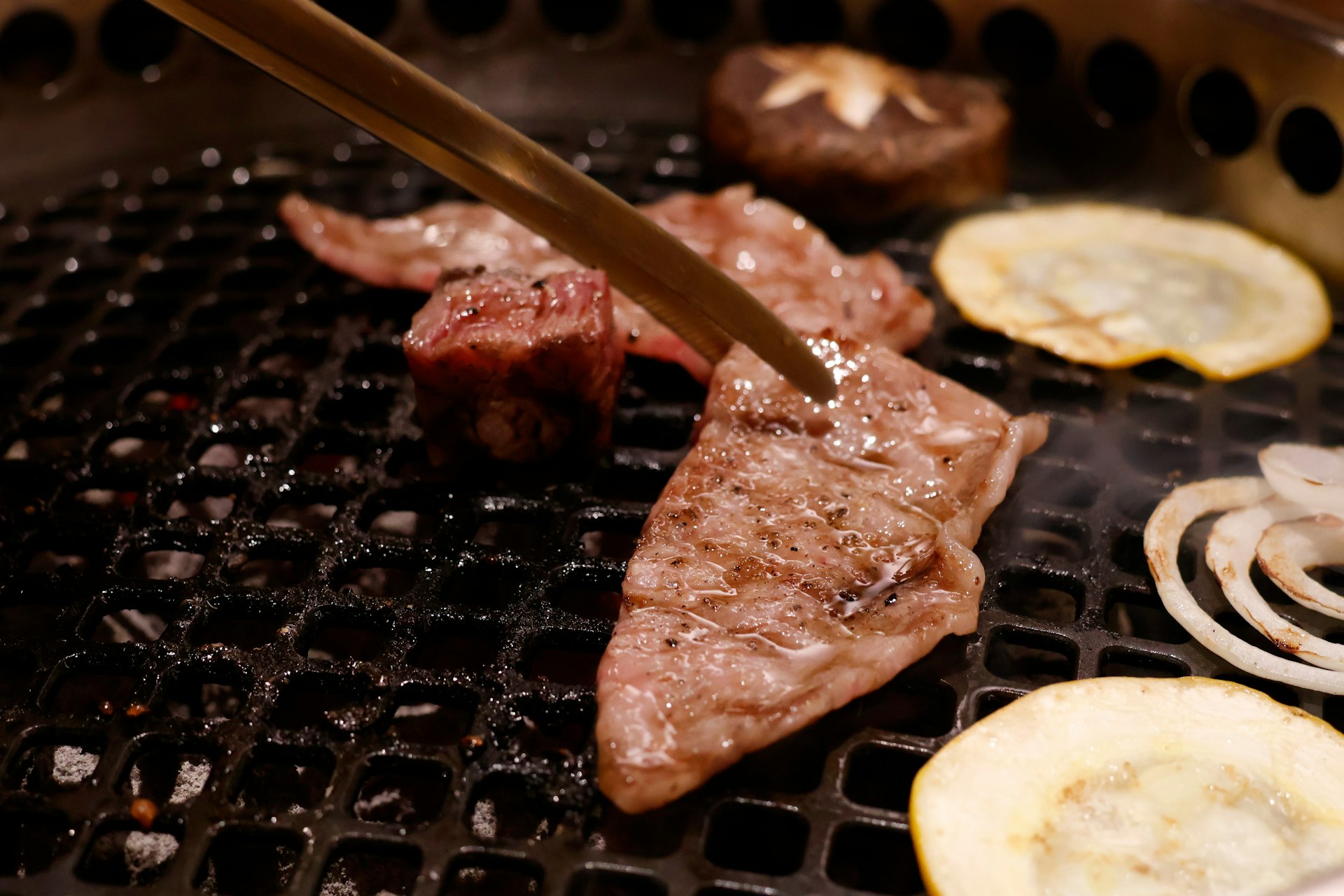 炭火の網の上で焼かれる霜降りの黒毛和牛とトング