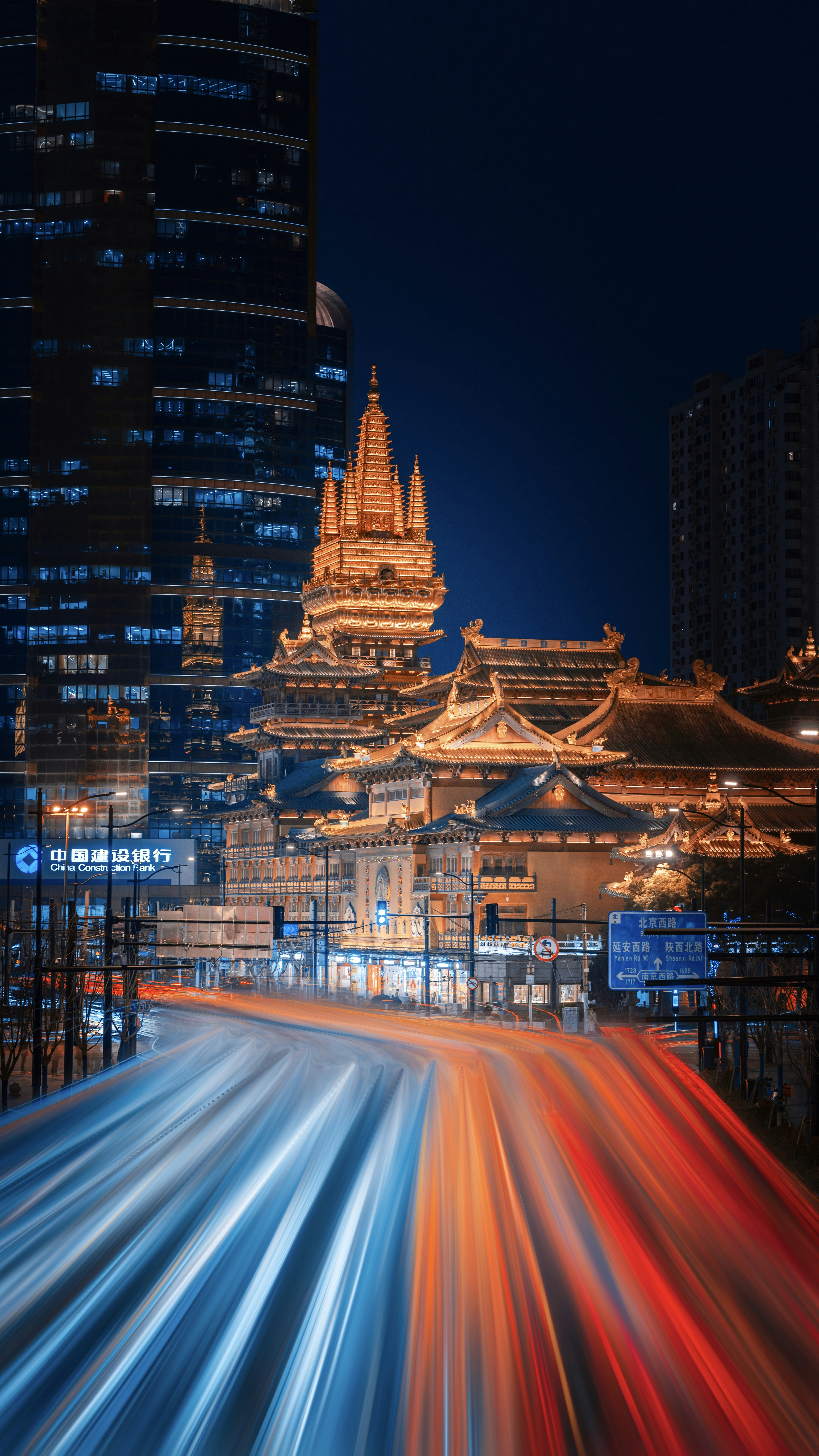 Cityscape at night with light trails and illuminated temple.