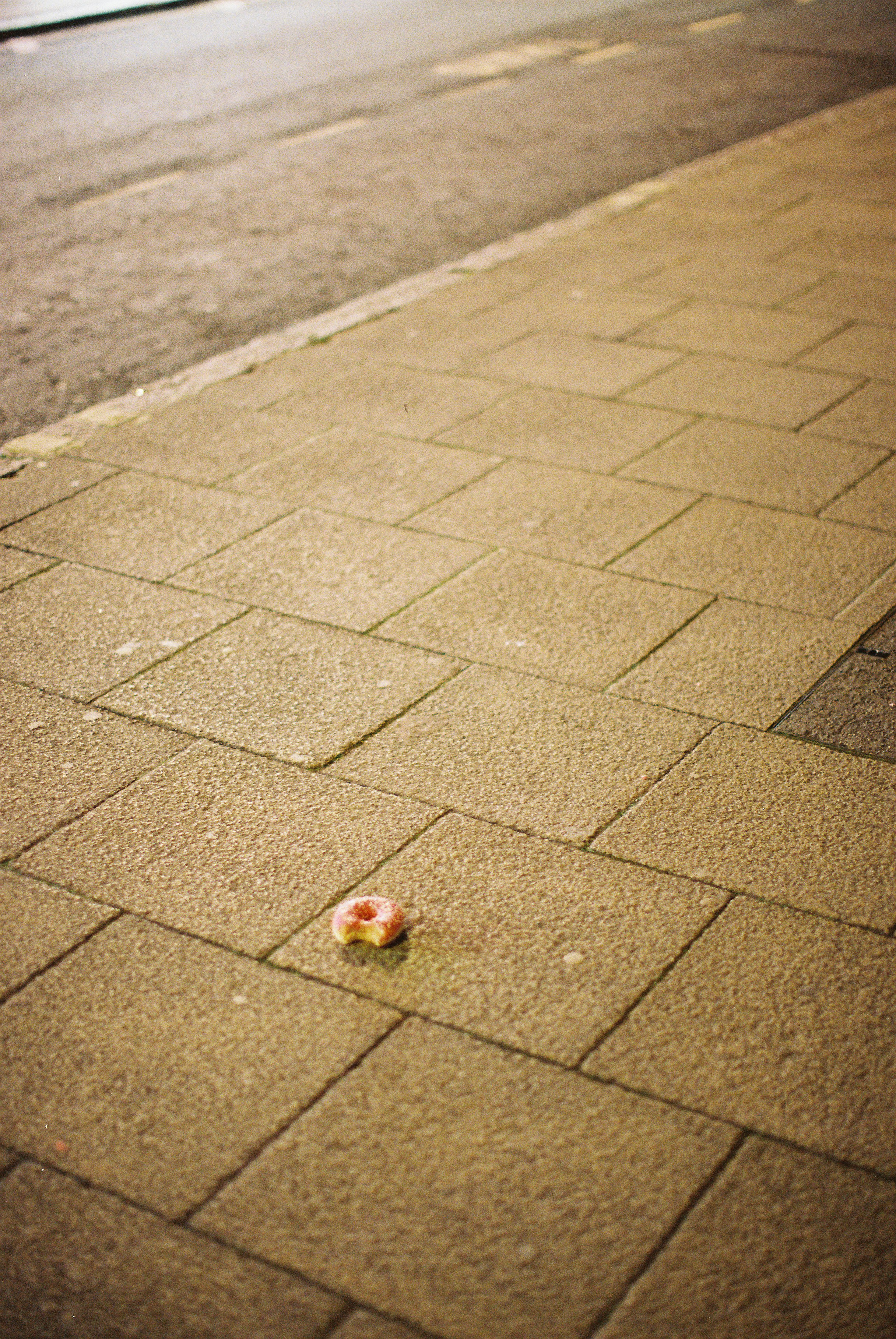 A single donut lies on a sidewalk
