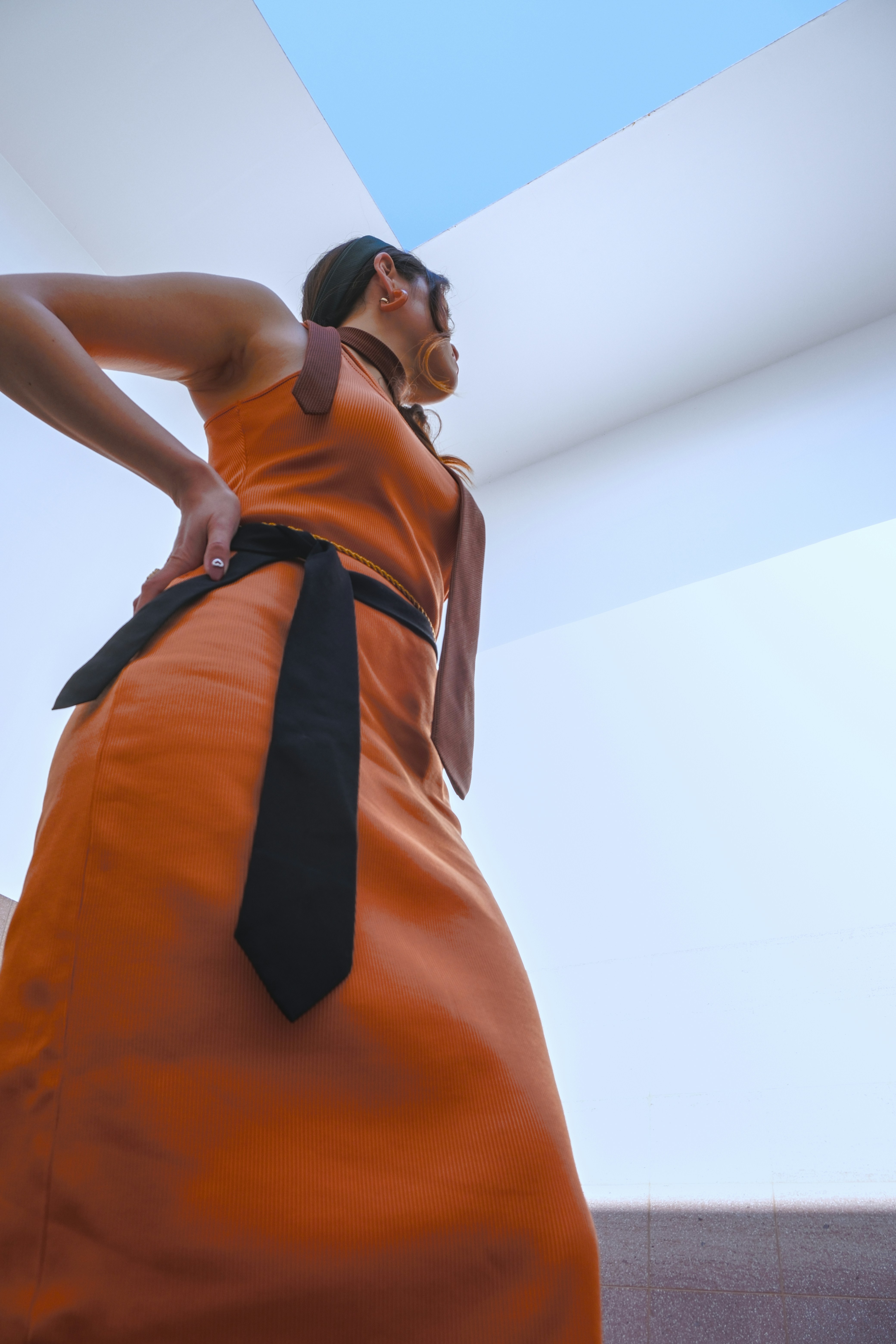 Frau im orangefarbenen Kleid mit schwarzer Schärpe blickt auf.