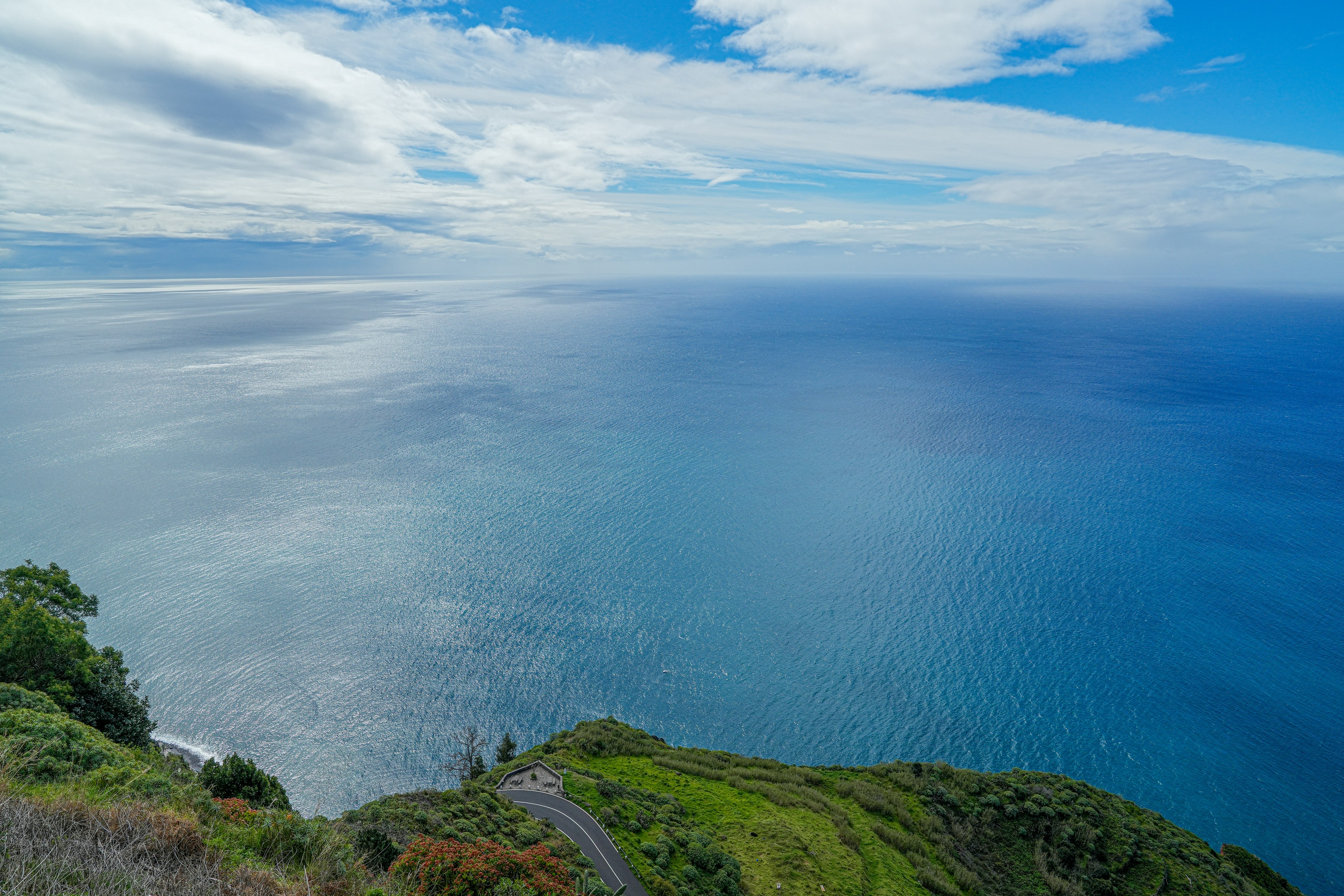 Vast blue ocean meeting a cloudy sky from a cliff.