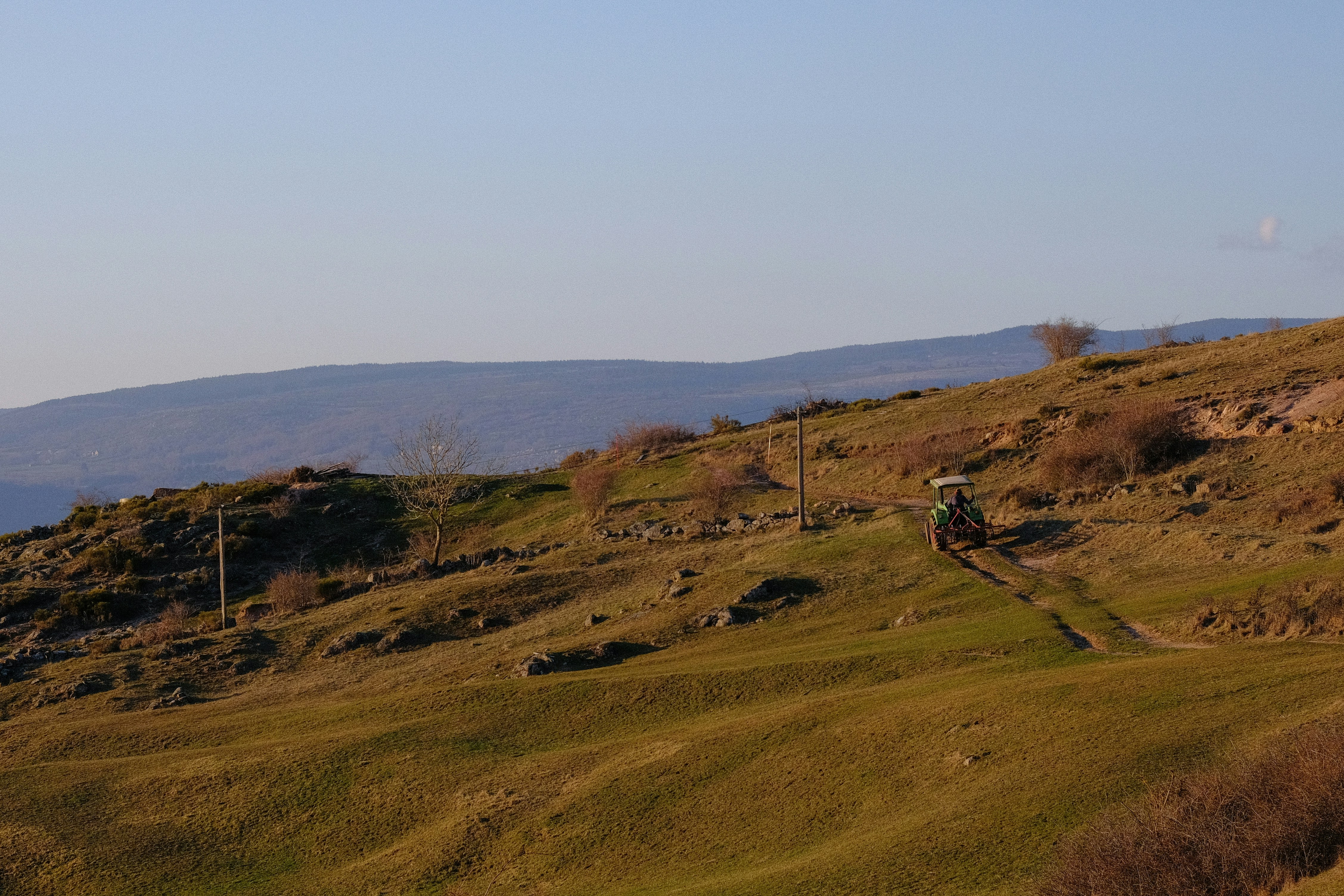 Tractor driving on a grassy hillside under a clear sky 풍경 사진