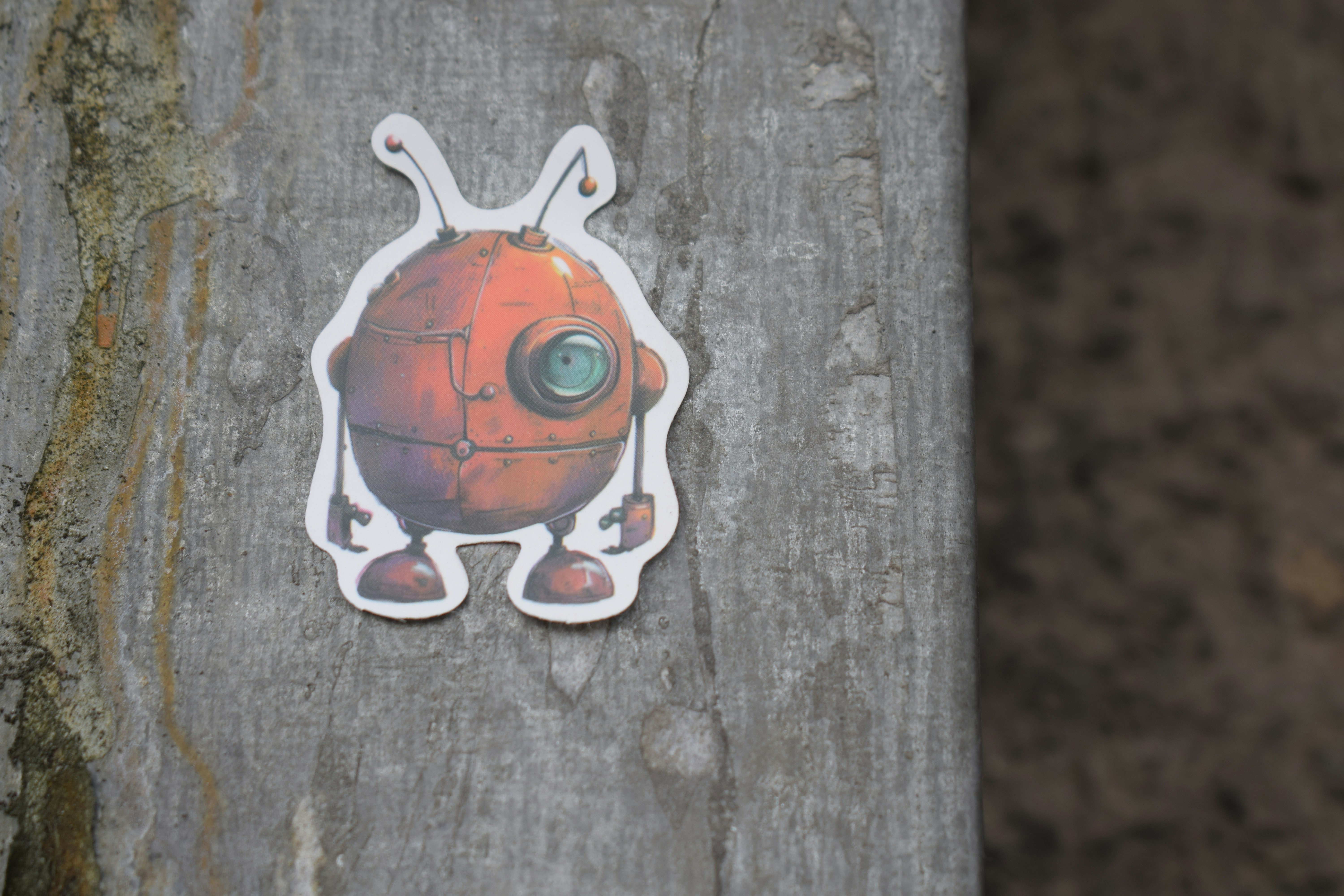 A small, round, red robot sticker on wood