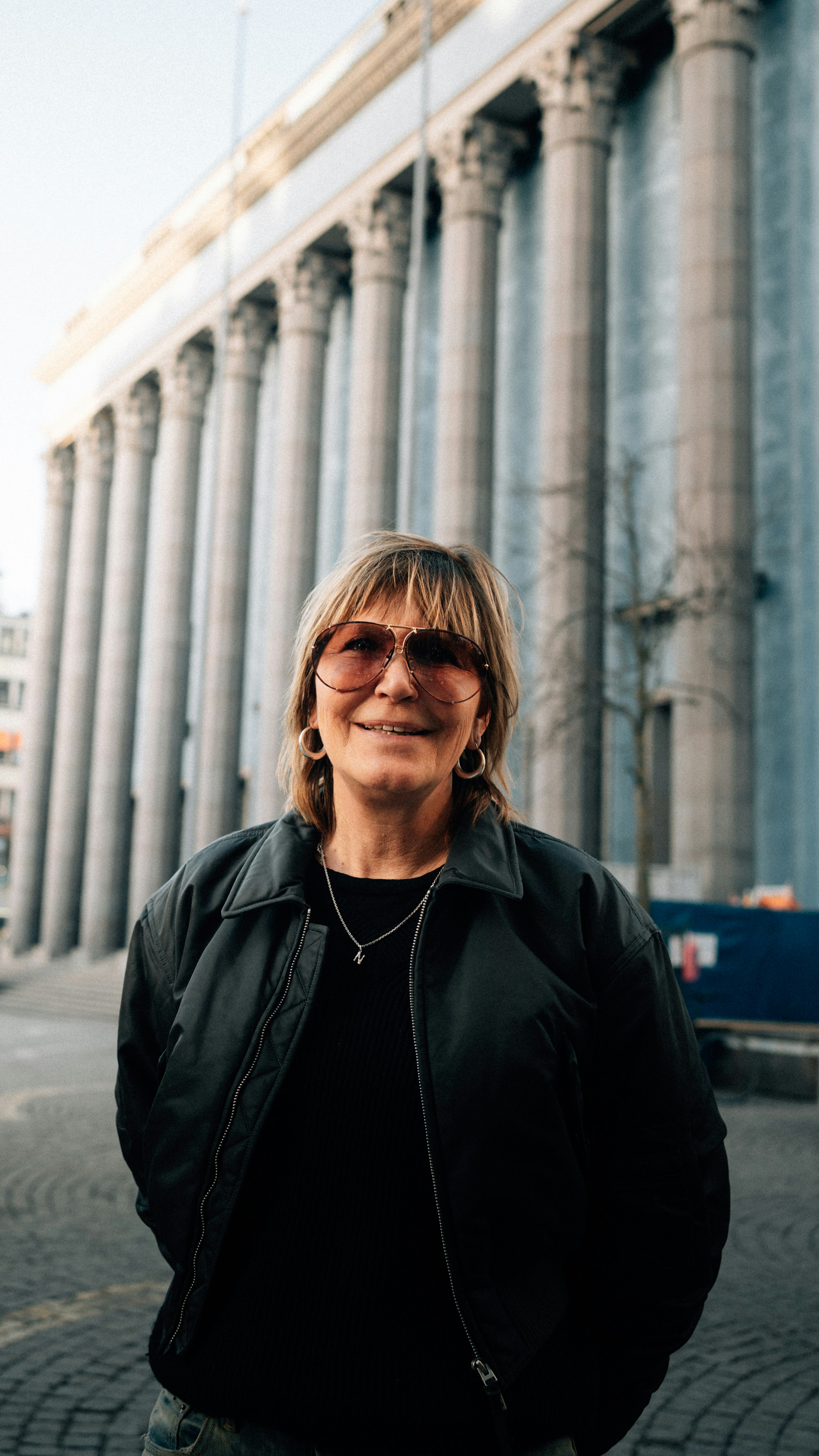 Woman in jacket standing in front of a grand building.