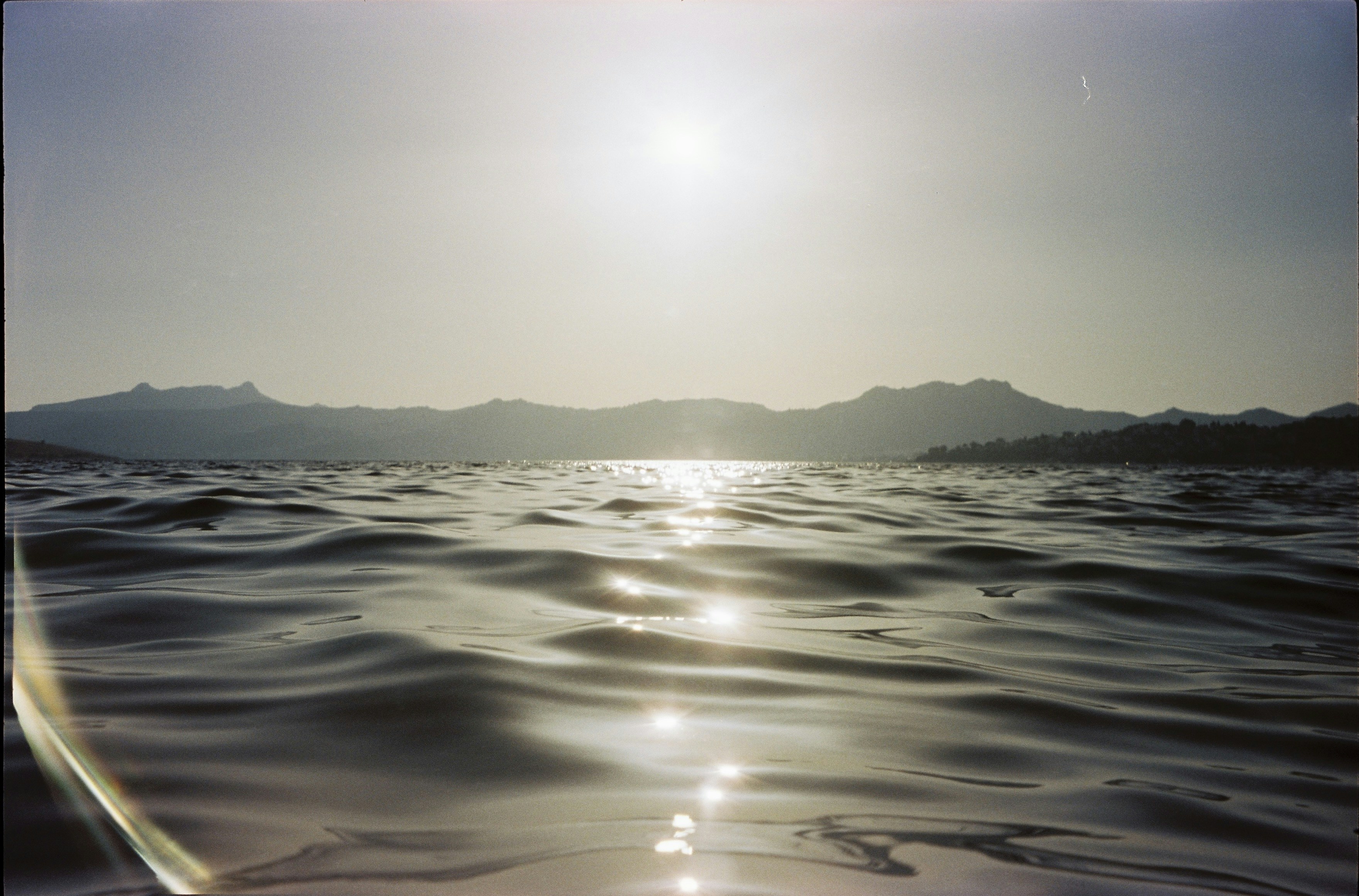 Sunlight glinting on rippling ocean water with distant mountains.