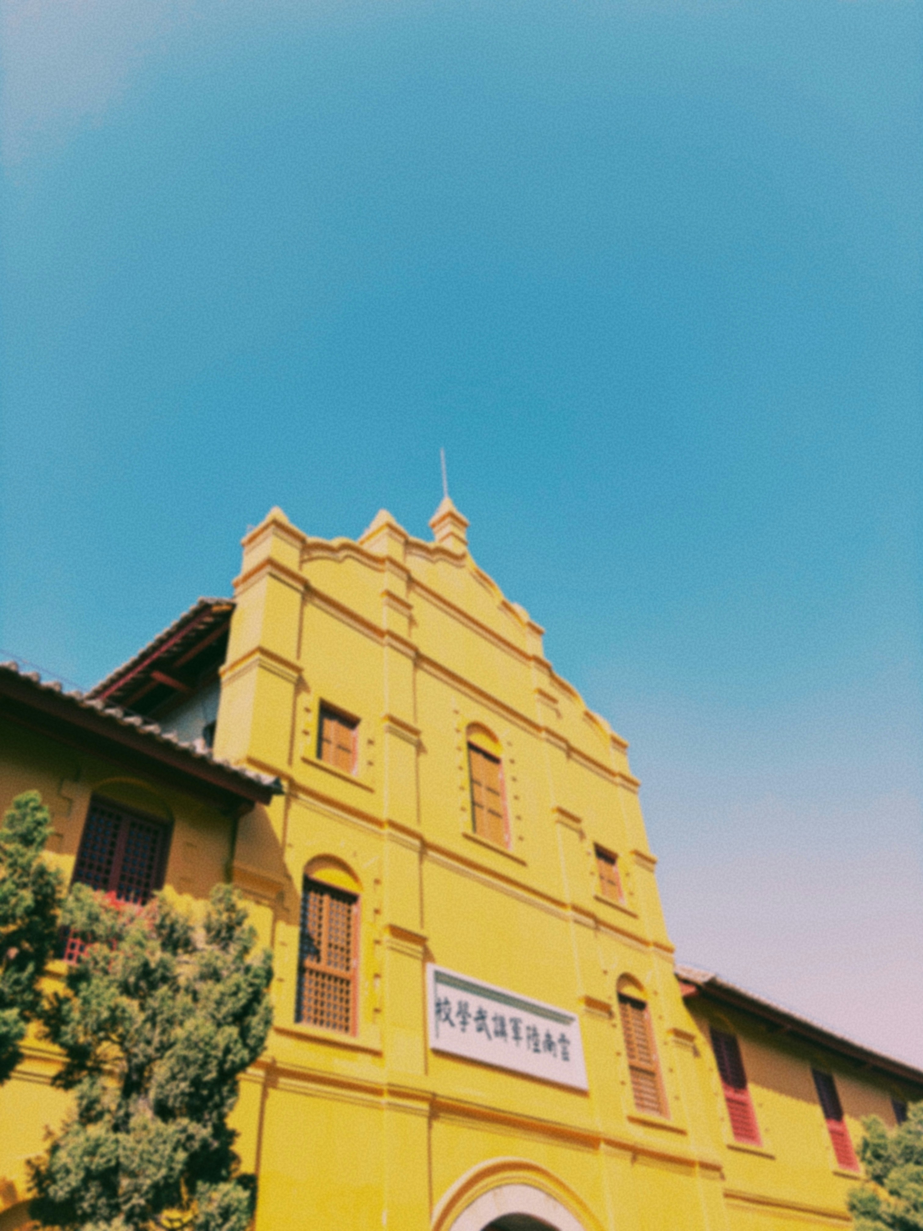 Prédio amarelo com céu azul e árvores
