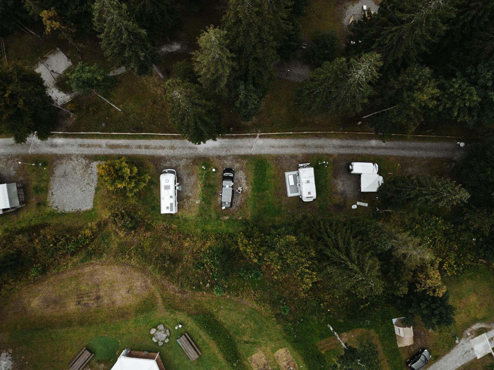 Overhead view of campground sites along a gravel loop road, with parked trailers, bare gravel pads, and trees between the sites