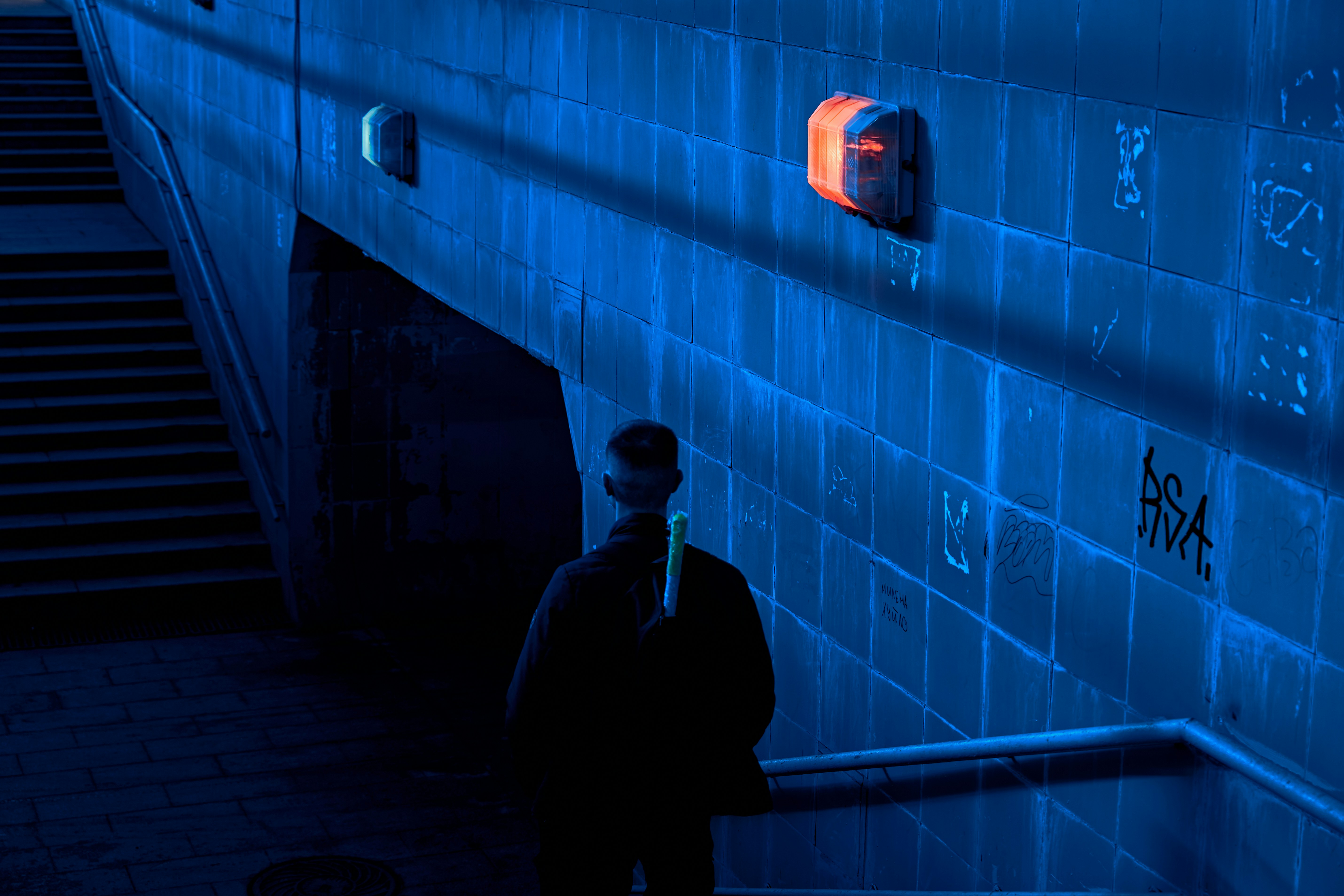 AI threat detection security - Man standing by a blue wall with graffiti at night.