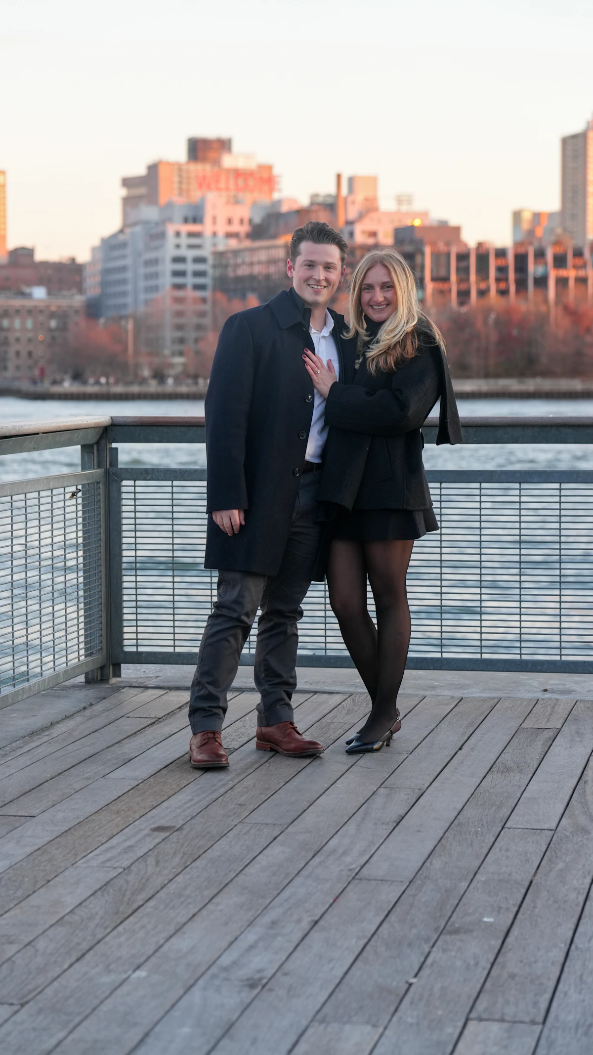 Olivia and Ethan on a wooden pier with the city behind them
