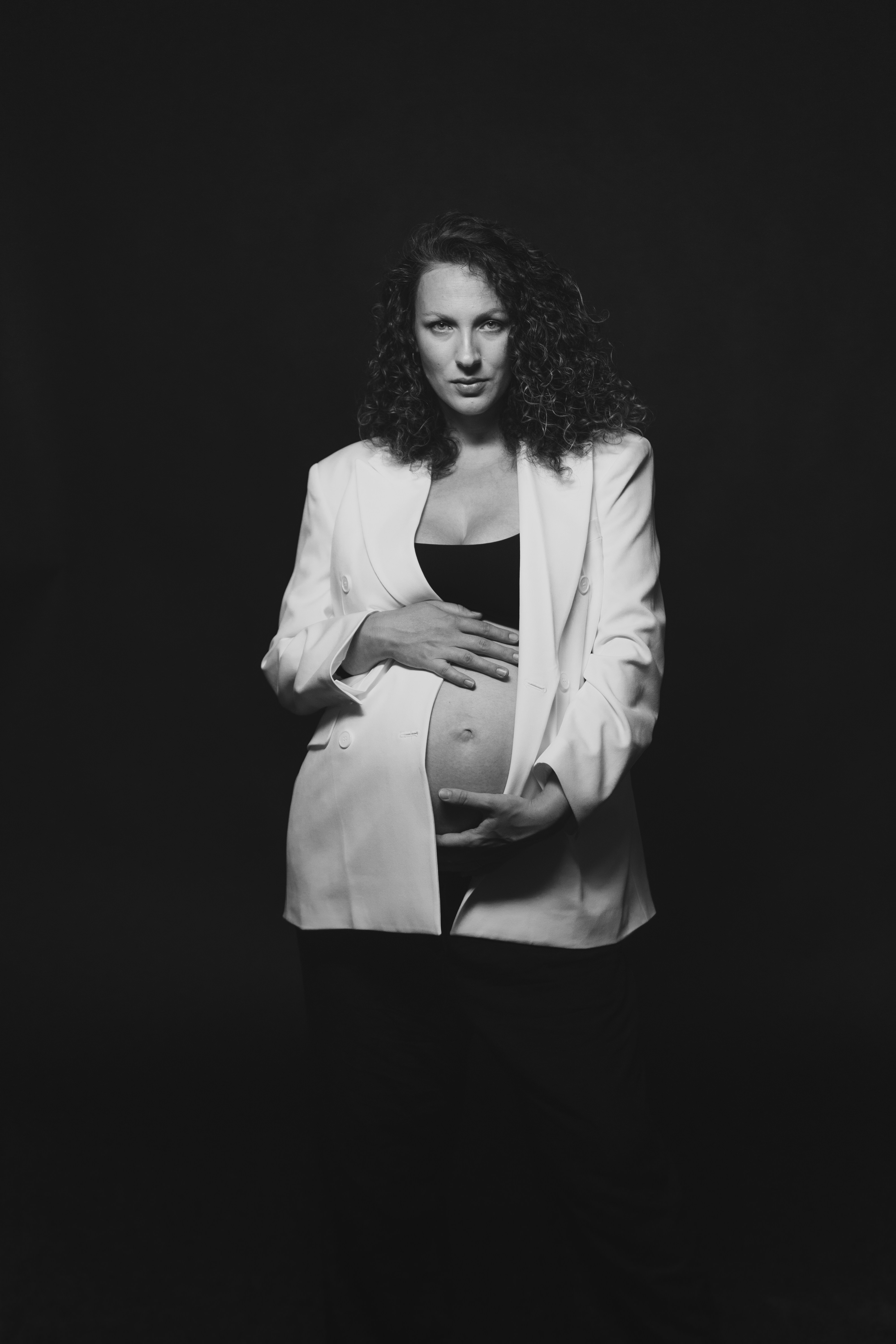 Donna incinta con una giacca bianca si tiene la pancia