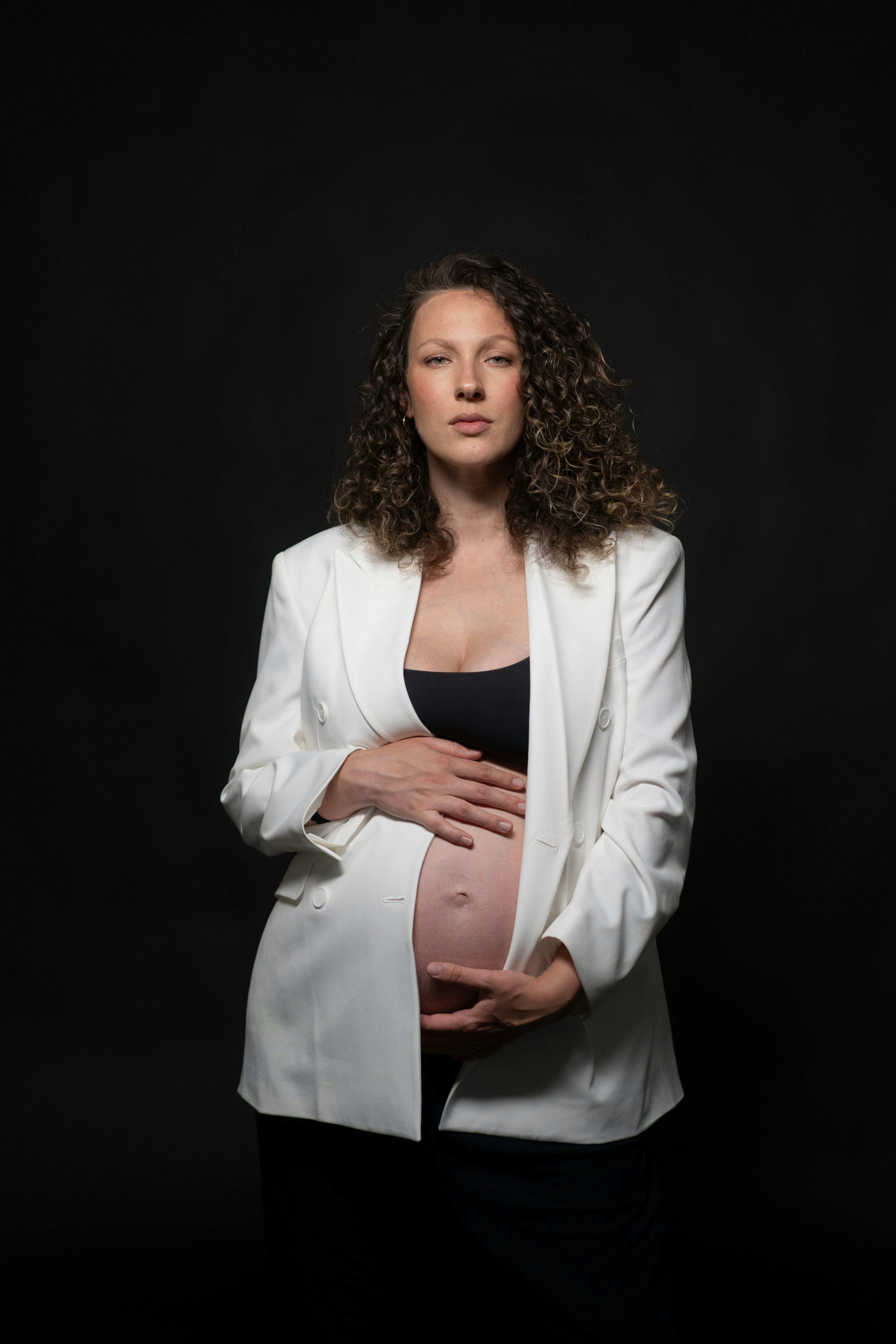 Pregnant woman in a white blazer holds her belly