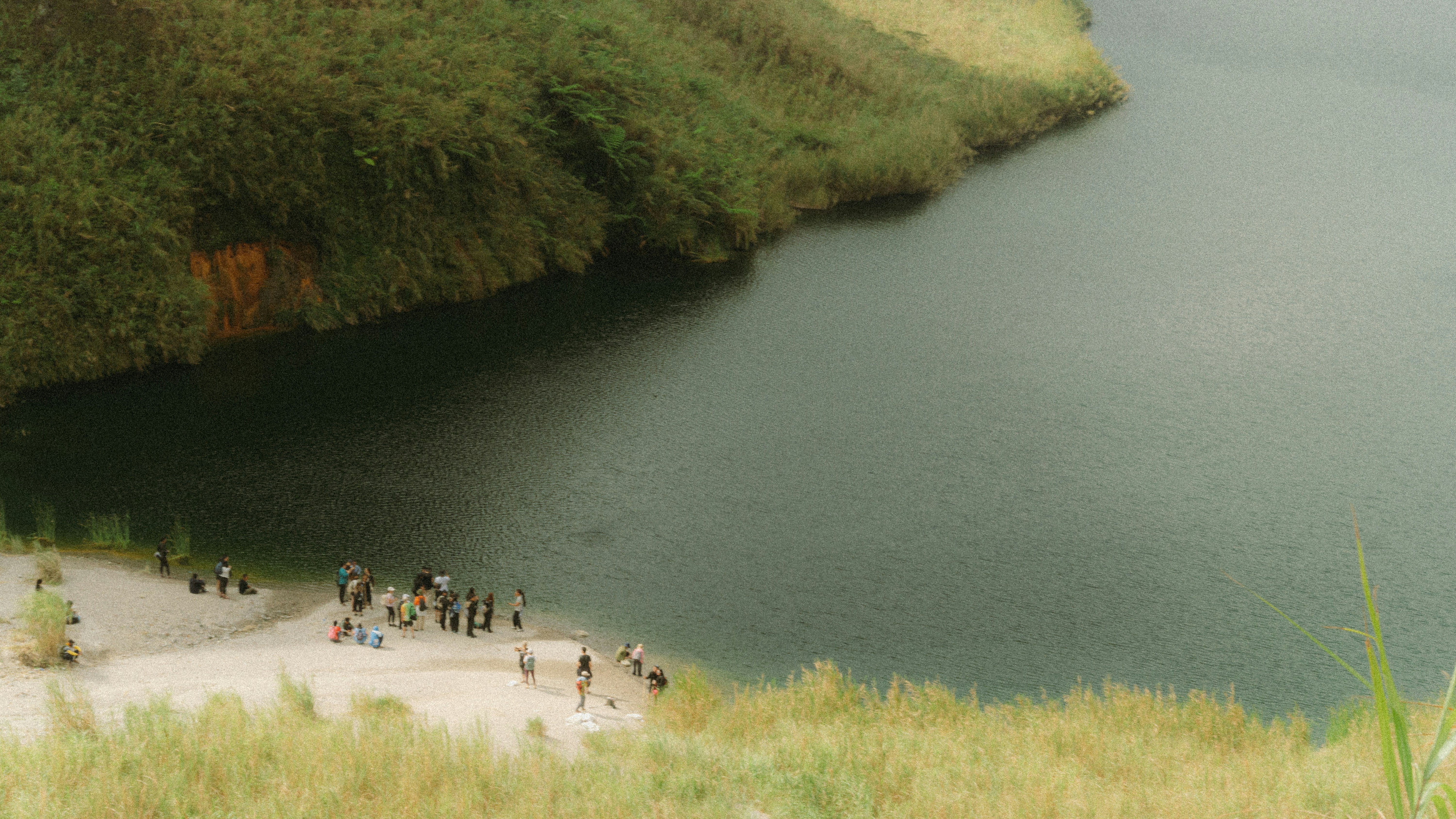 People gathered on a sandy shore next to a lake