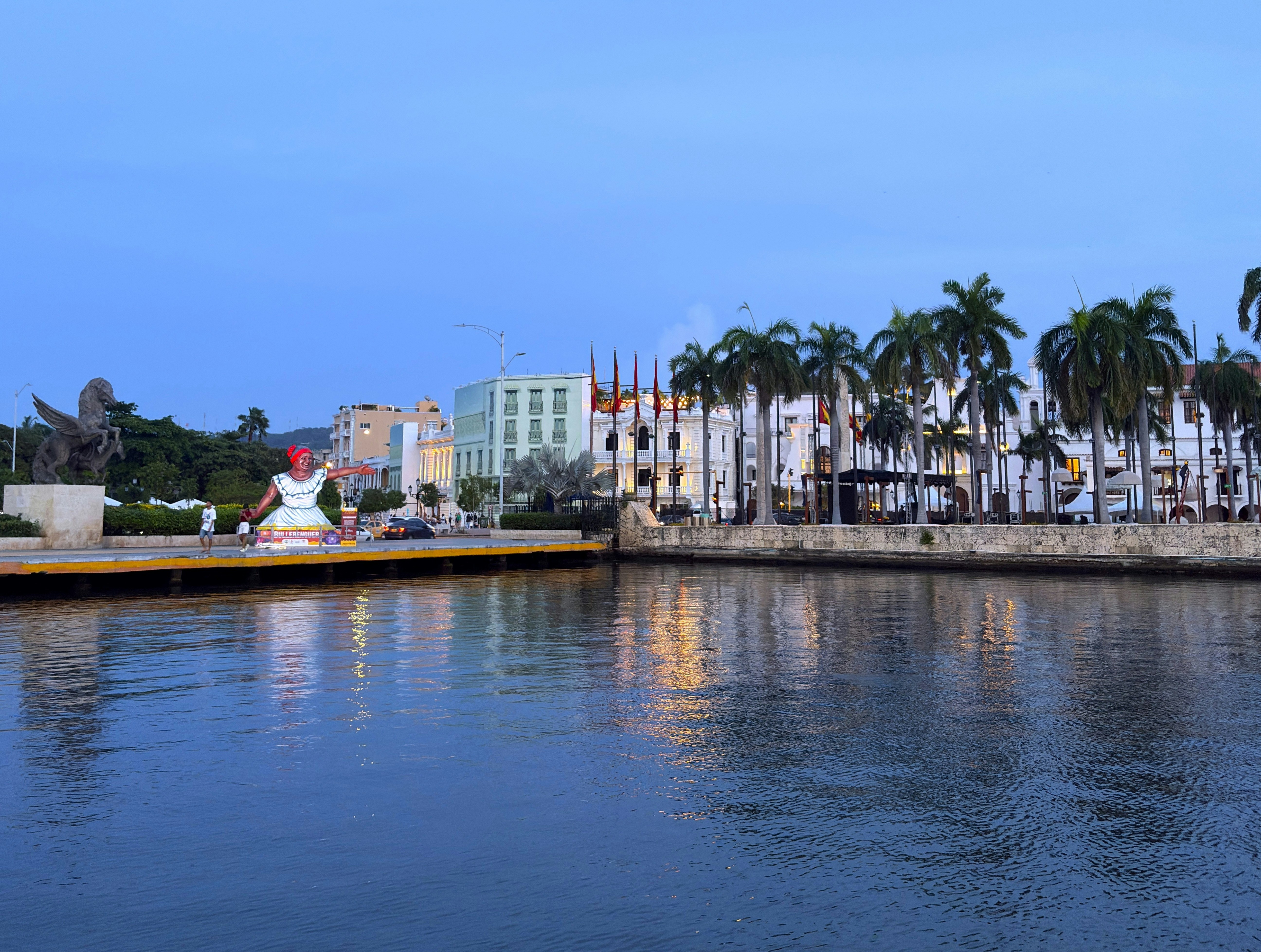 Waterfront buildings with palm trees and a statue.