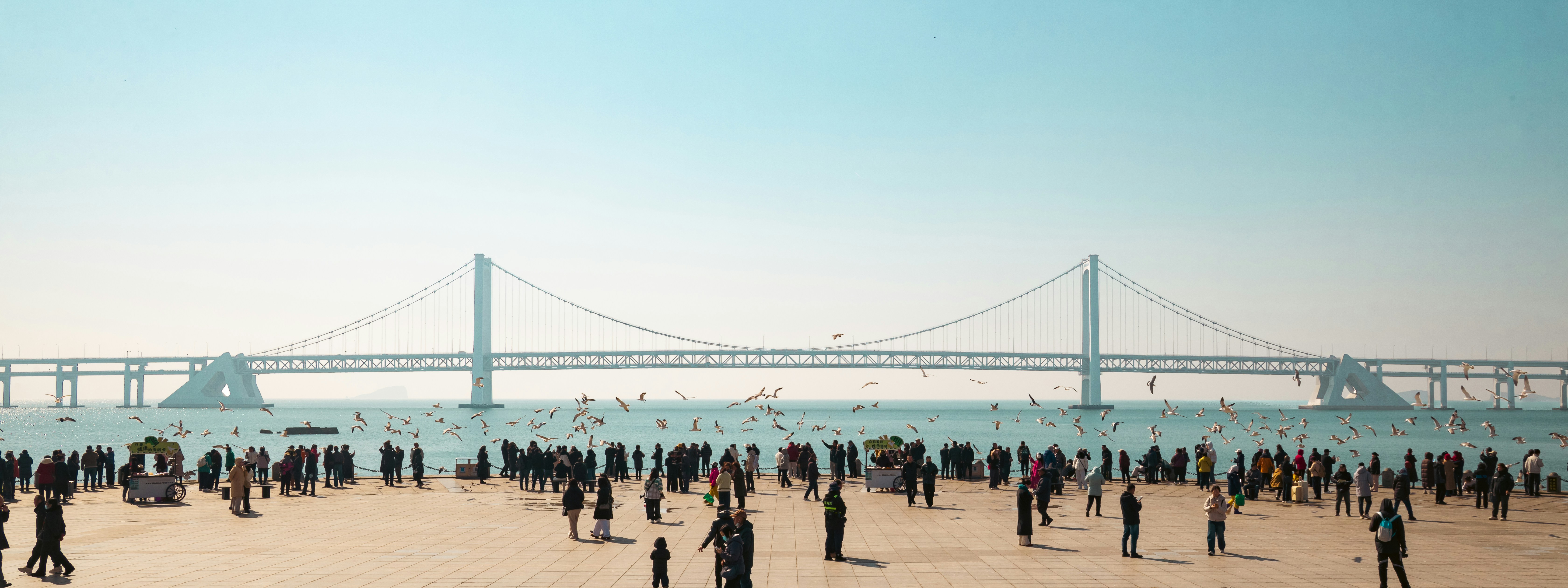 Gente en la playa con puente colgante de fondo