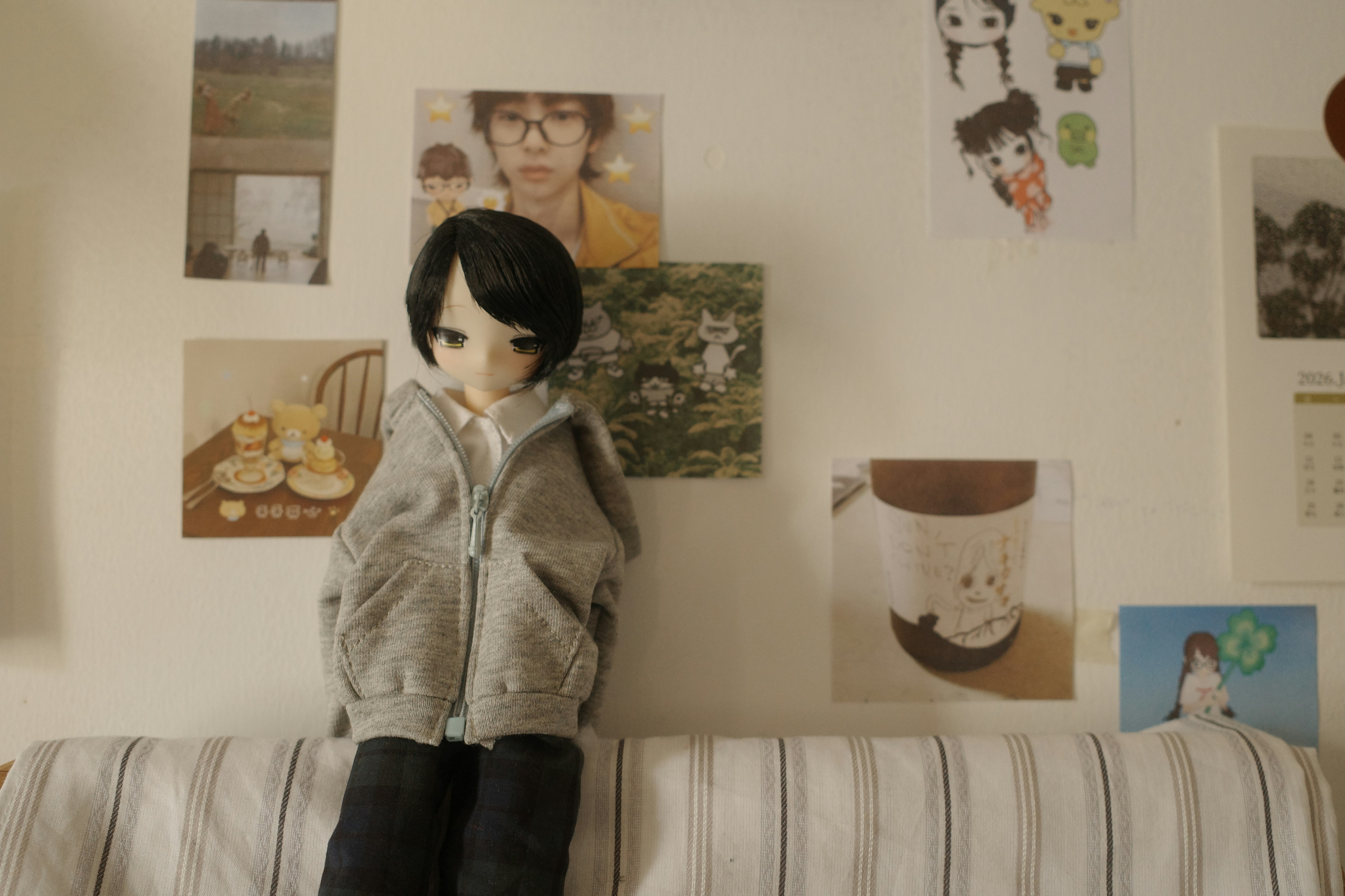 Doll wearing a hoodie sits on a striped couch.