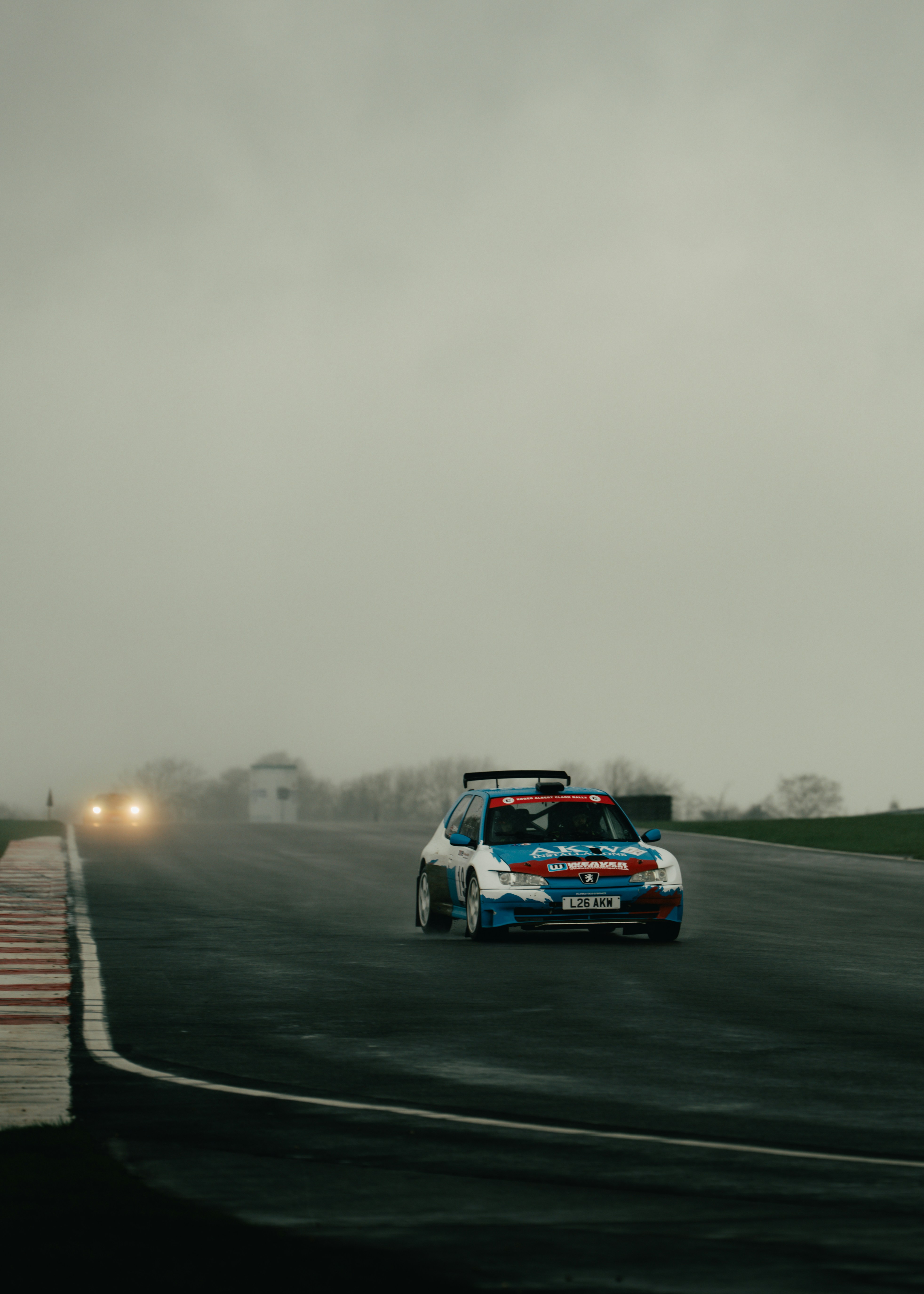 Rally car races on a wet track under cloudy skies