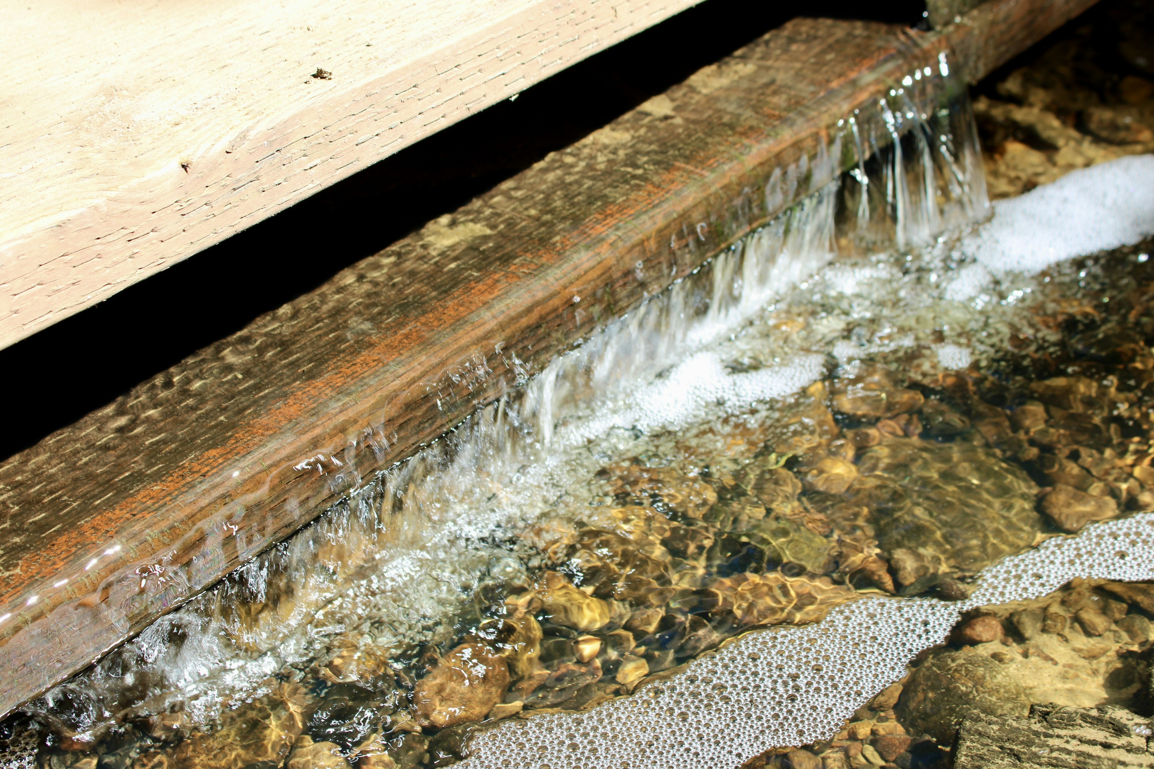 Water flows over a wooden plank into a rocky stream.