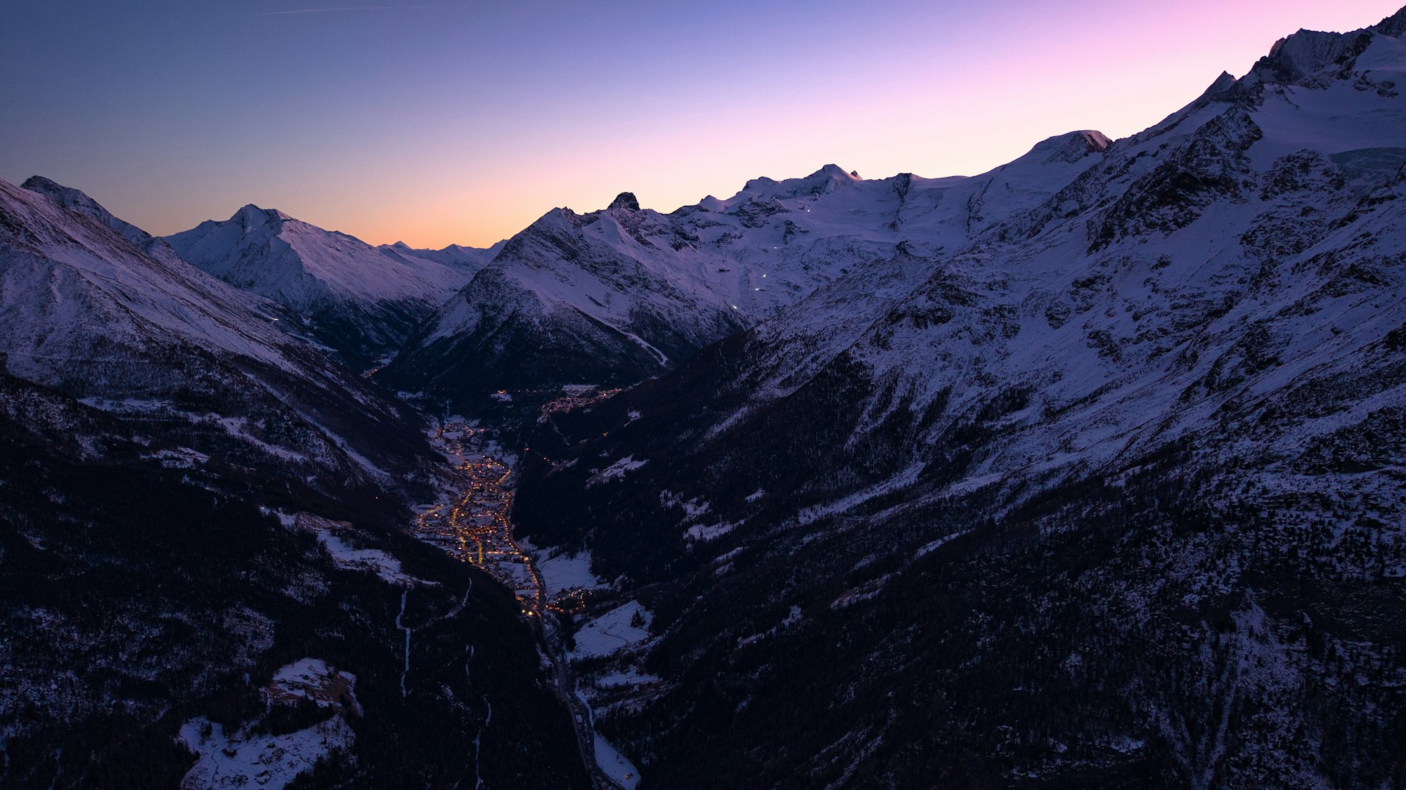 Snowy mountain valley with illuminated Austrian alpine village at dusk