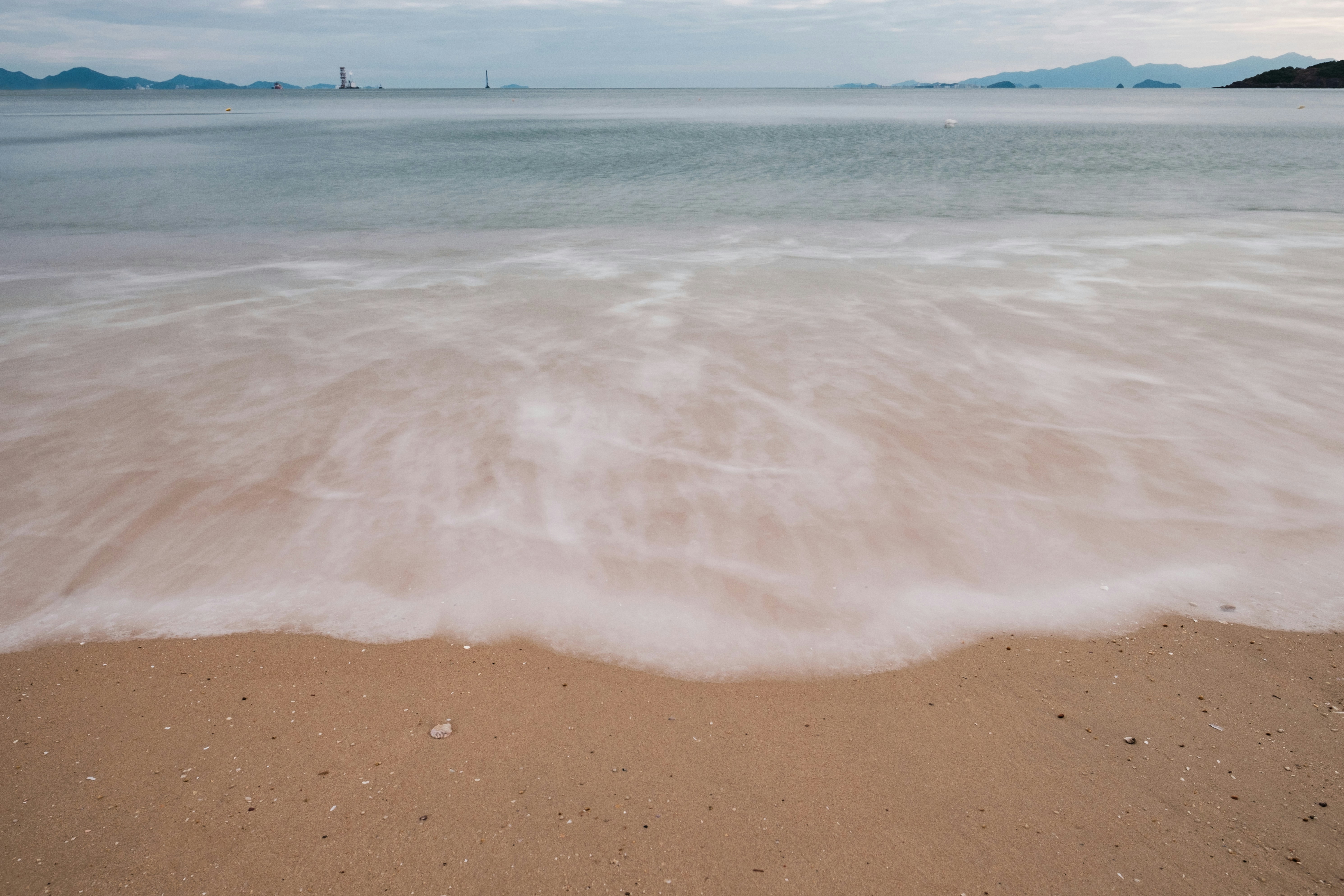 Olas suaves bañan una playa de arena al anochecer.