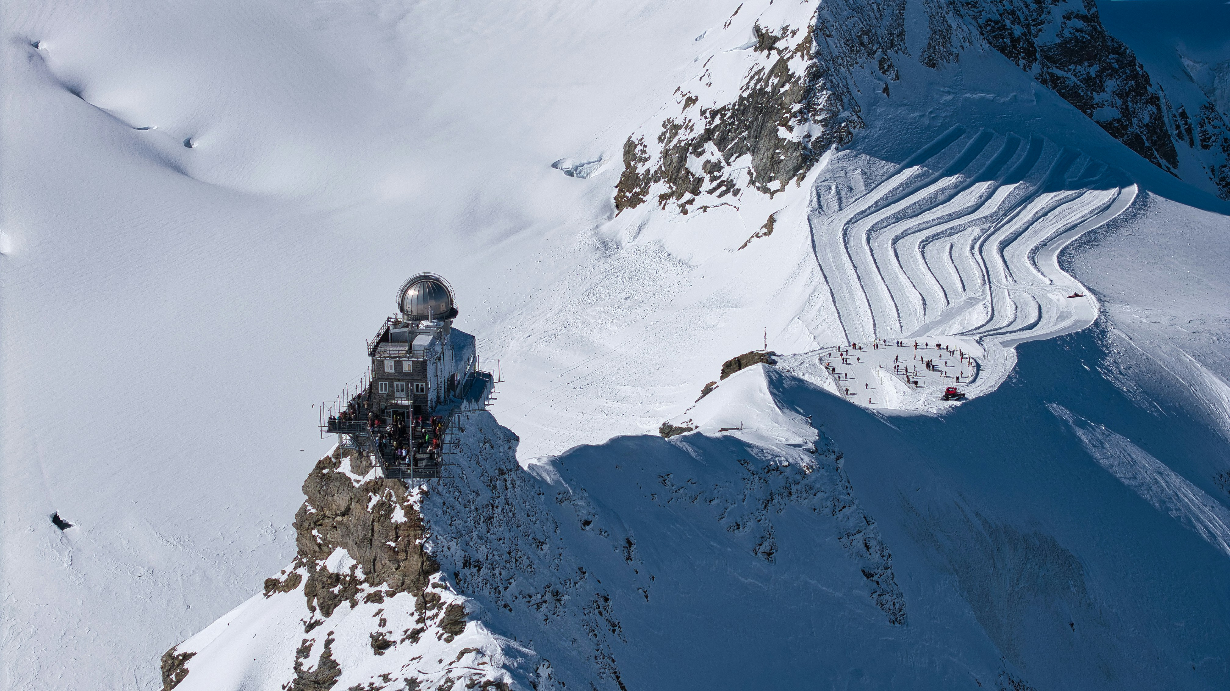 A futuristic building sits on a snowy mountain peak.