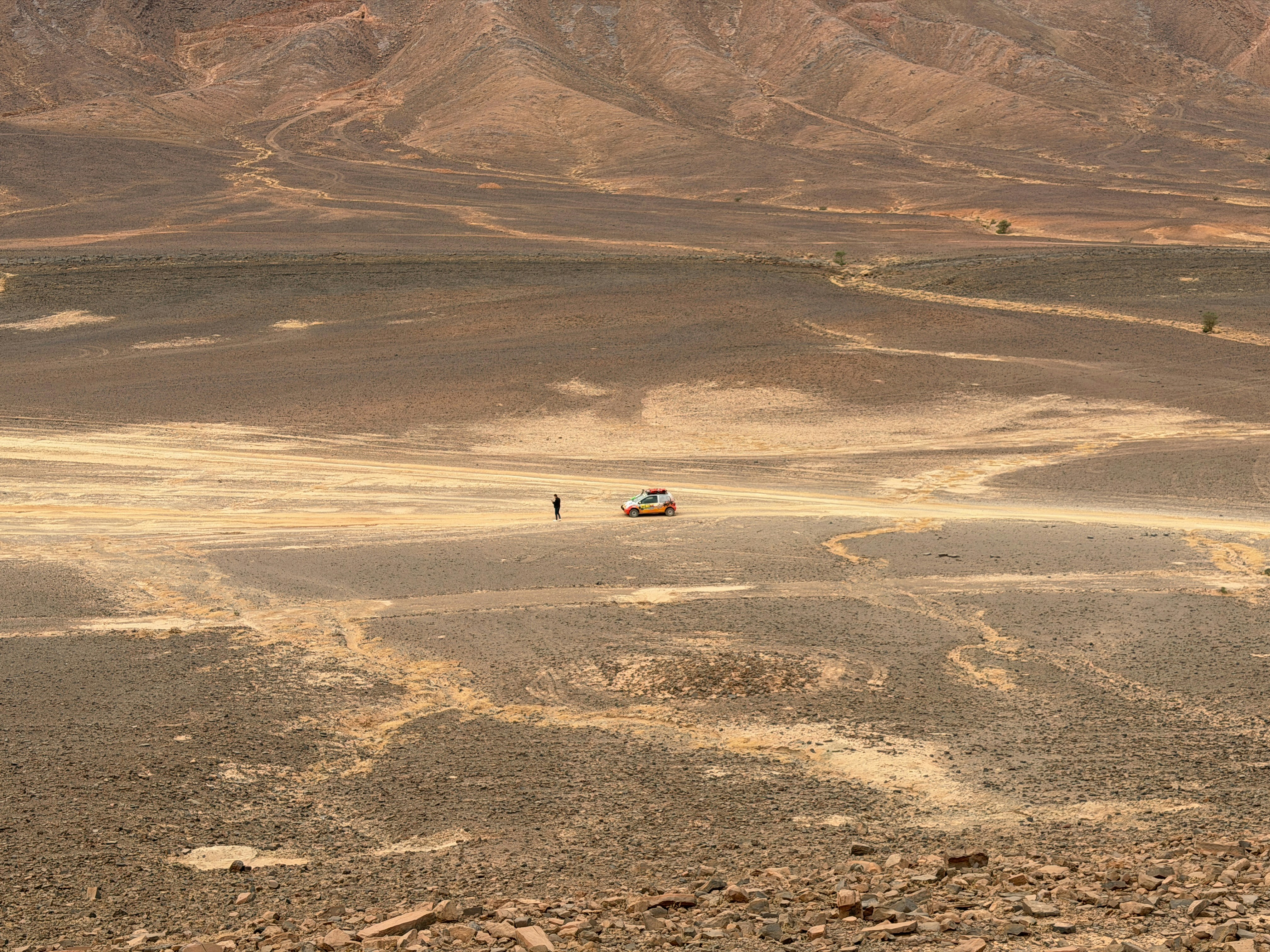A lone figure and vehicle in a vast desert landscape.