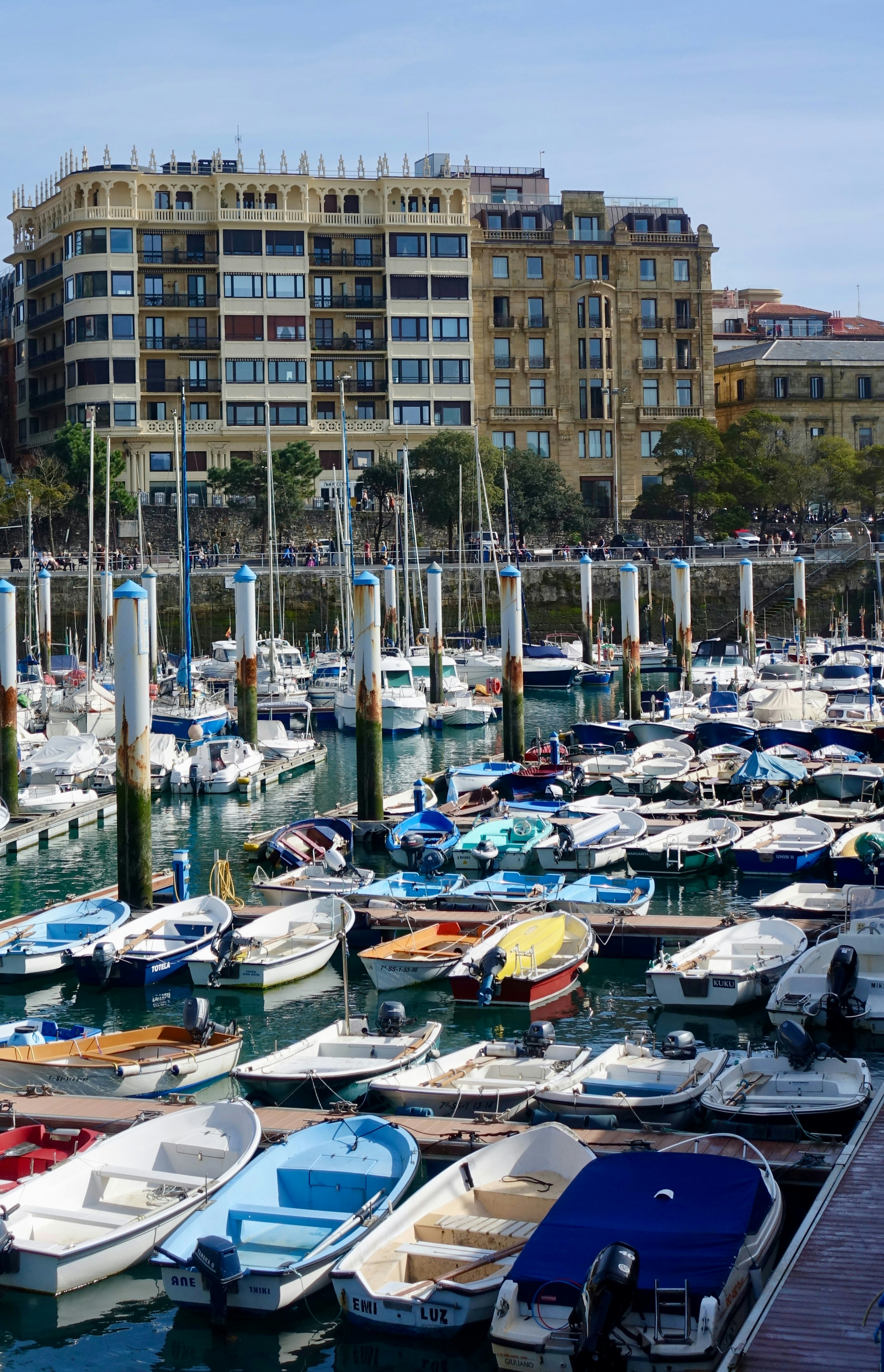 Many boats docked in a harbor with buildings behind.