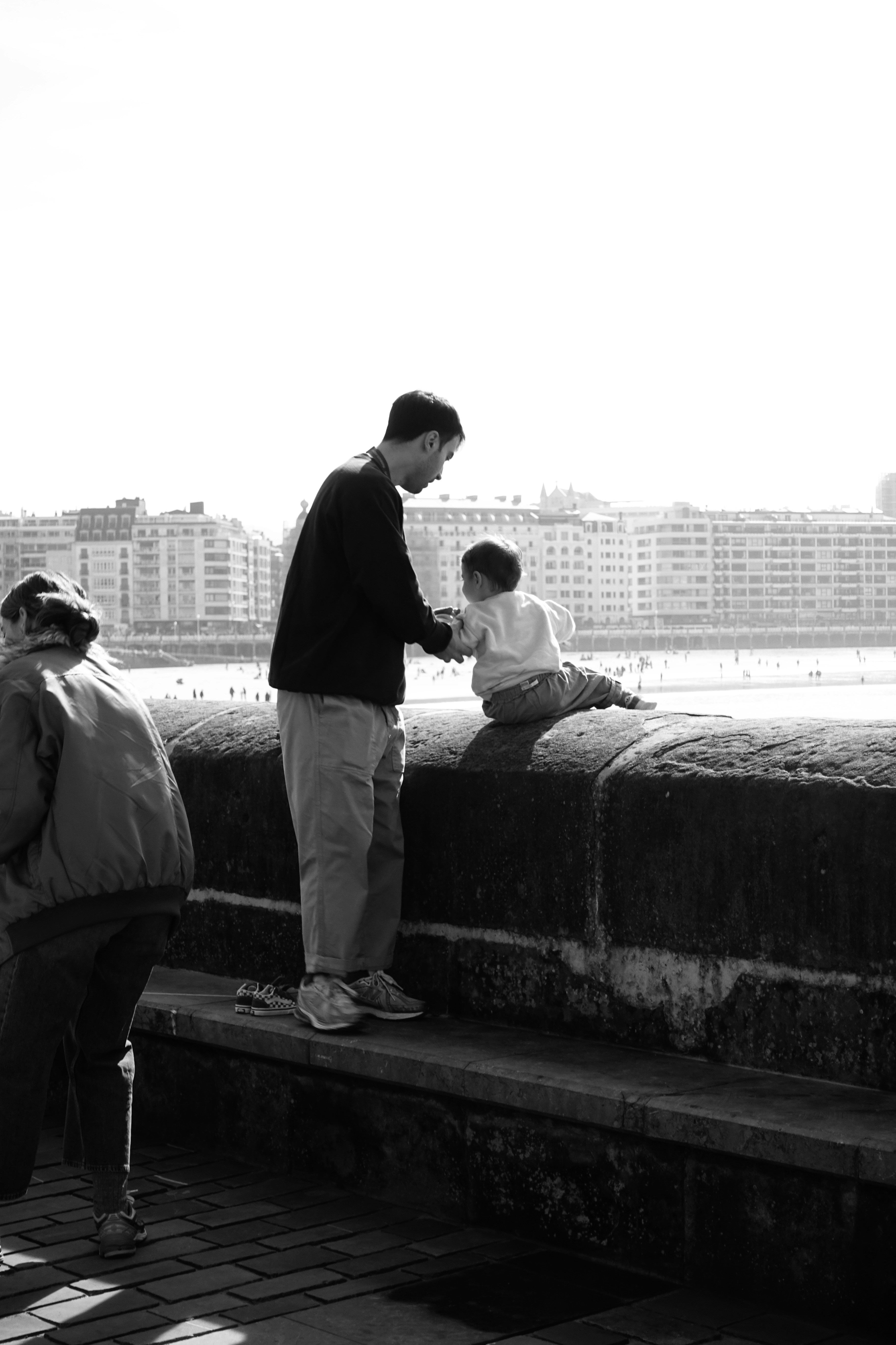 Man and child interact by a stone wall overlooking beach.