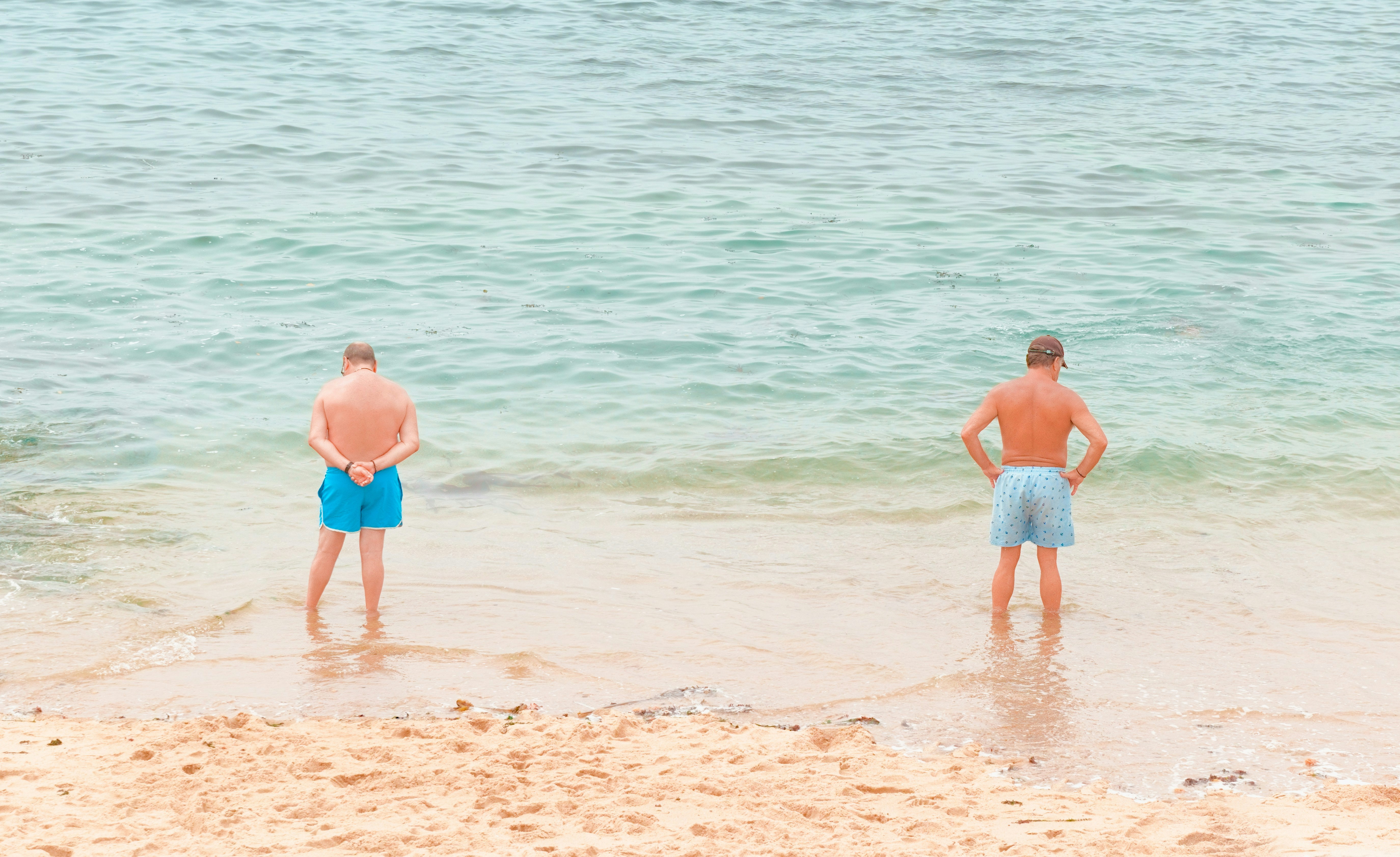 Two men standing on a sandy beach by the ocean.