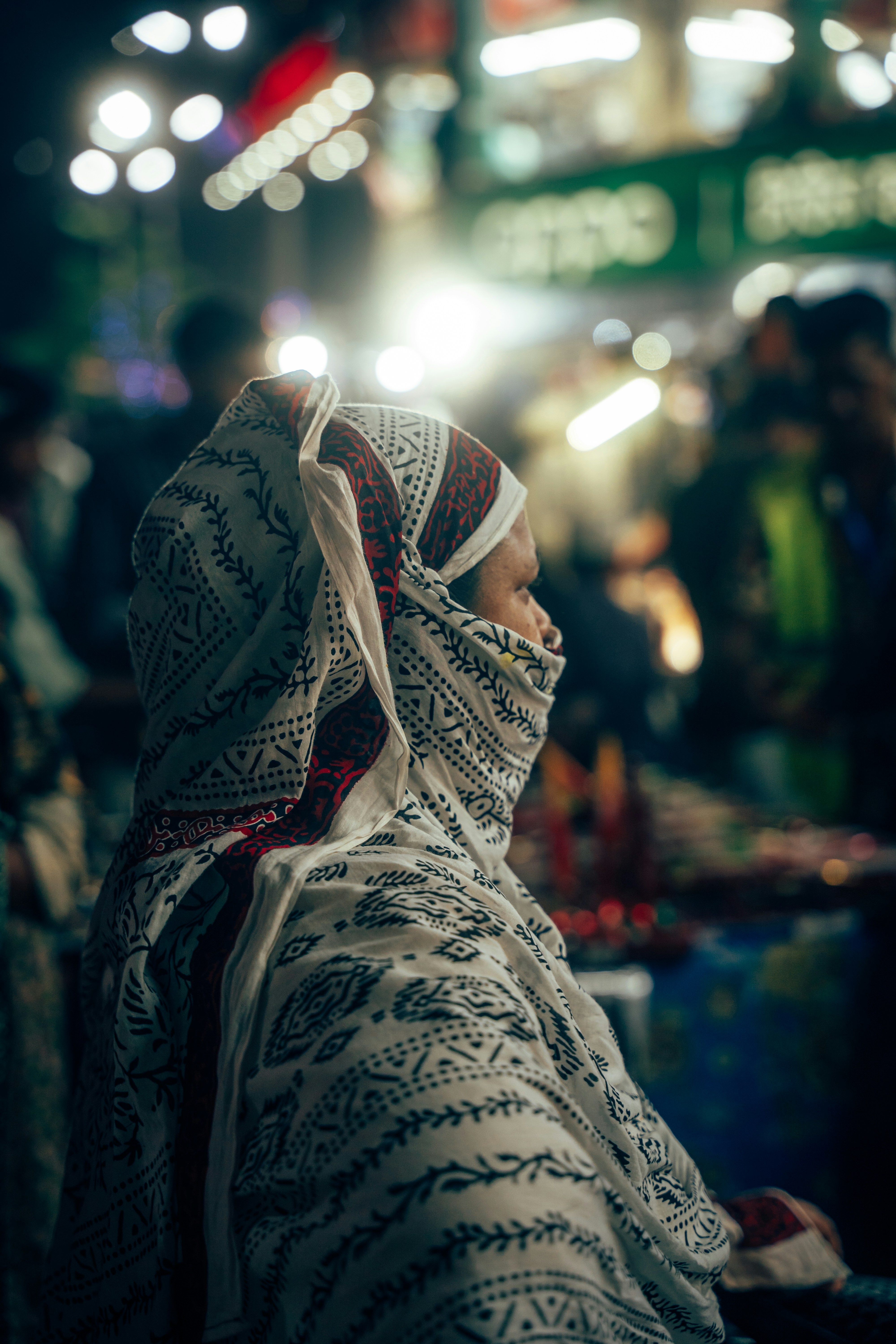 Femme en foulard traditionnel dans un marché nocturne animé.