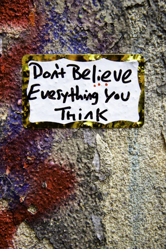 Sticker on textured wall reads 'don't believe everything you think'.